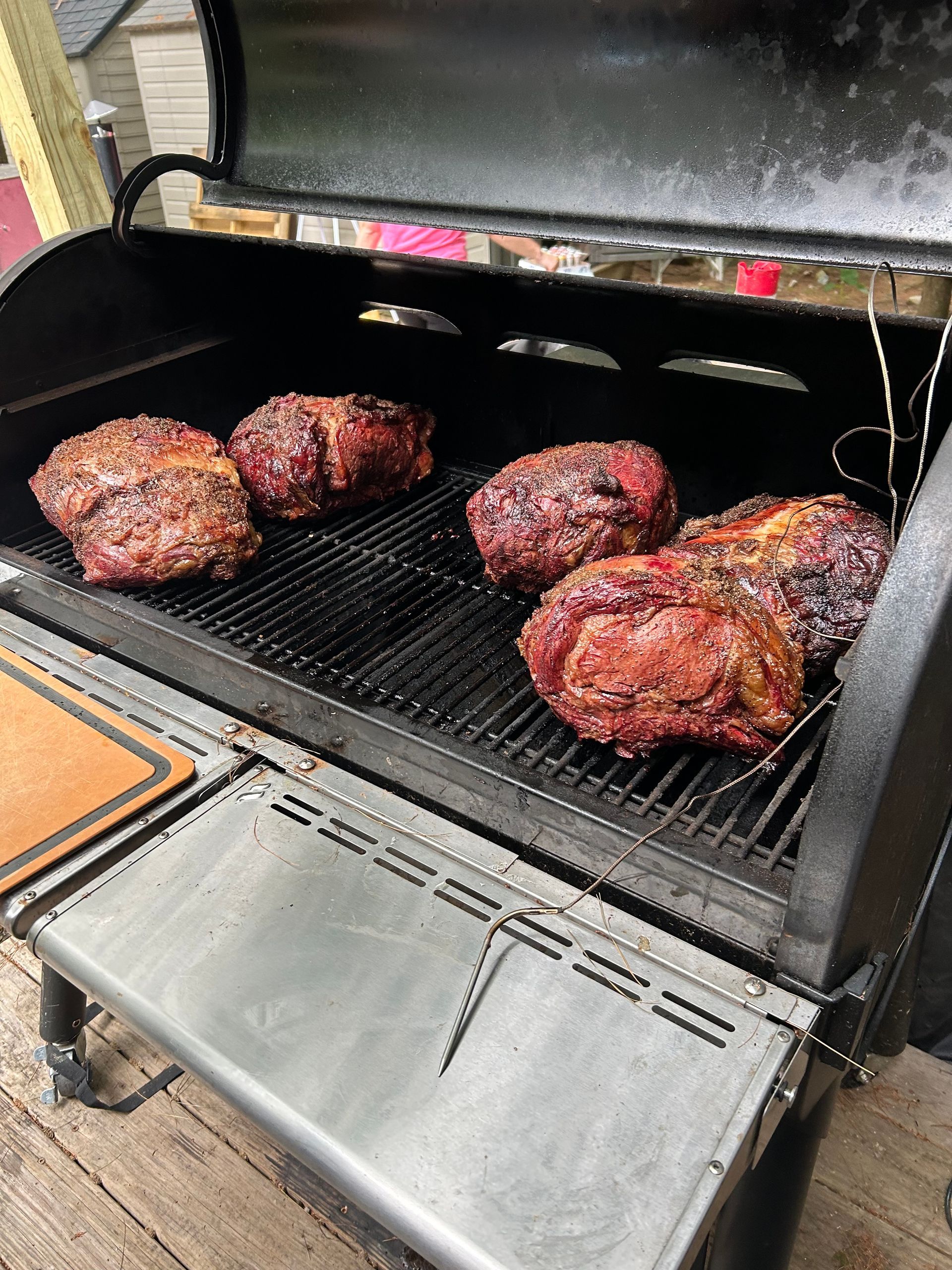 A grill with meat on it is sitting on a wooden deck.
