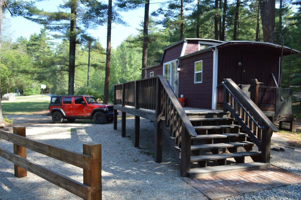 A red jeep is parked in front of a trailer with stairs leading up to it.