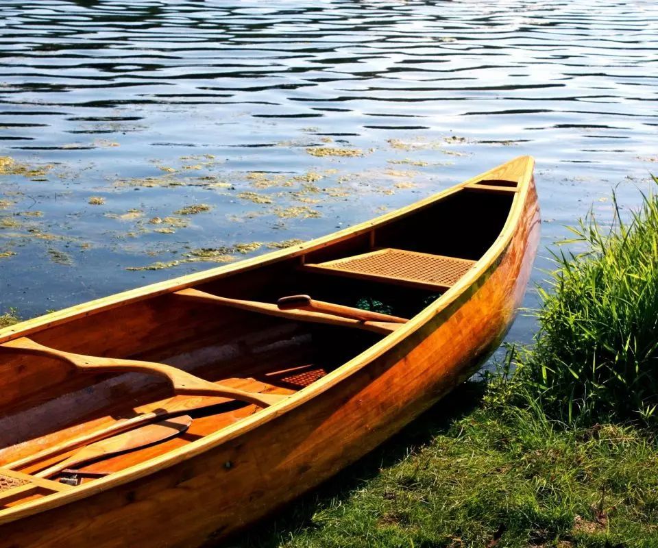 A wooden canoe is sitting on the shore of a lake