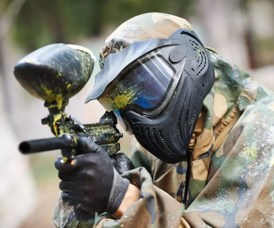 A man wearing a helmet and goggles is playing paintball.