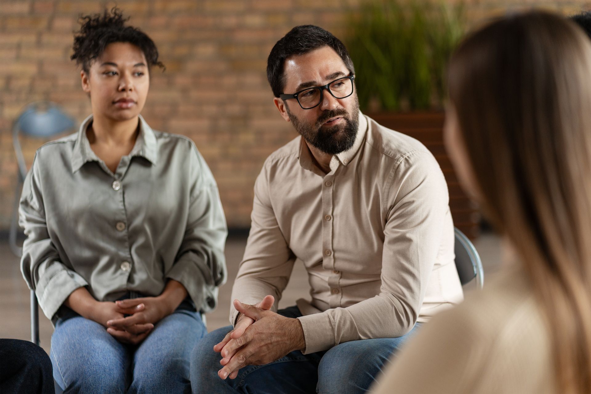 People in a group therapy session, seated in chairs, listening attentively.