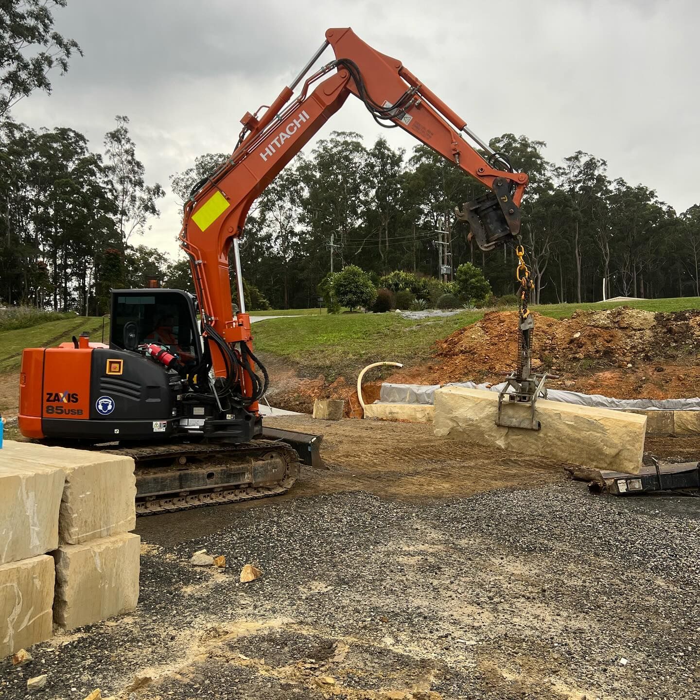 Orange Hitachi Excavator Lifting a Sandstone Block — MG Earthworks and Plant Hire in Kempsey, NSW