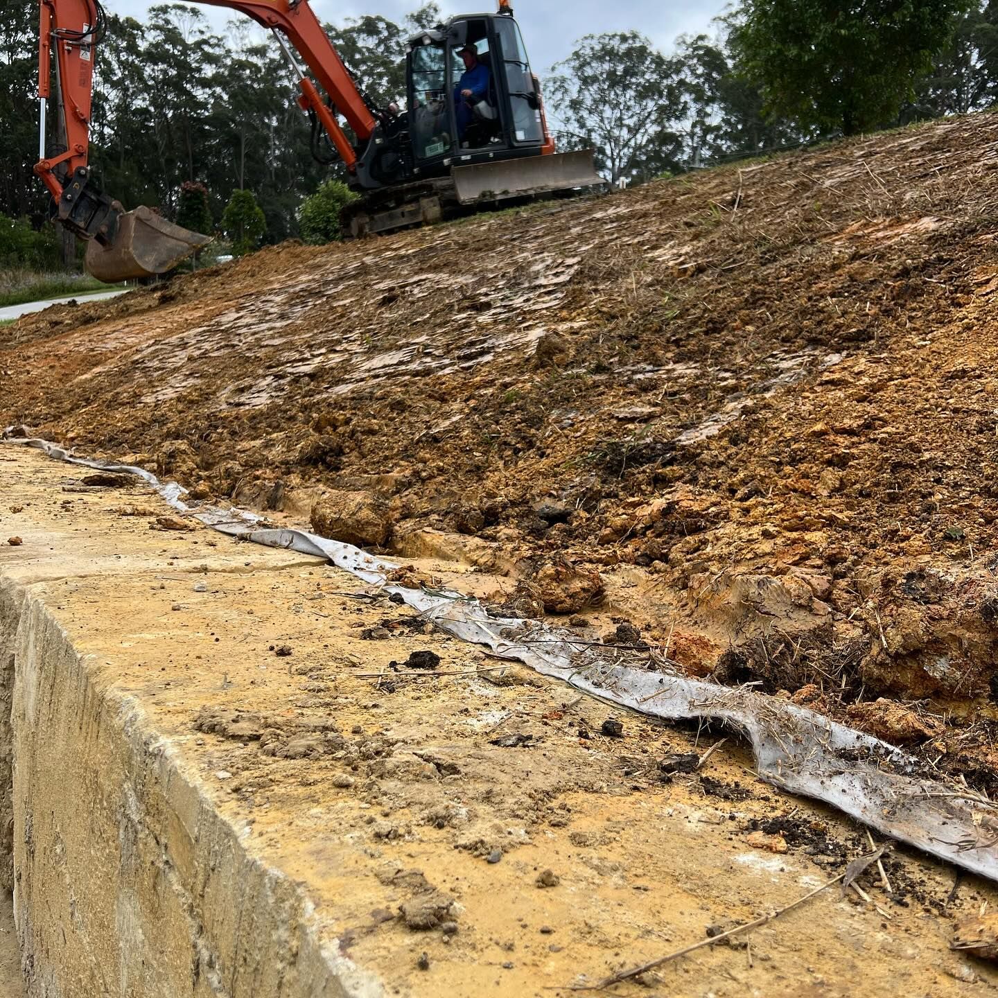 Excavator on a Muddy Hillside, Working Near a Concrete Barrier — MG Earthworks and Plant Hire in Macksville, NSW