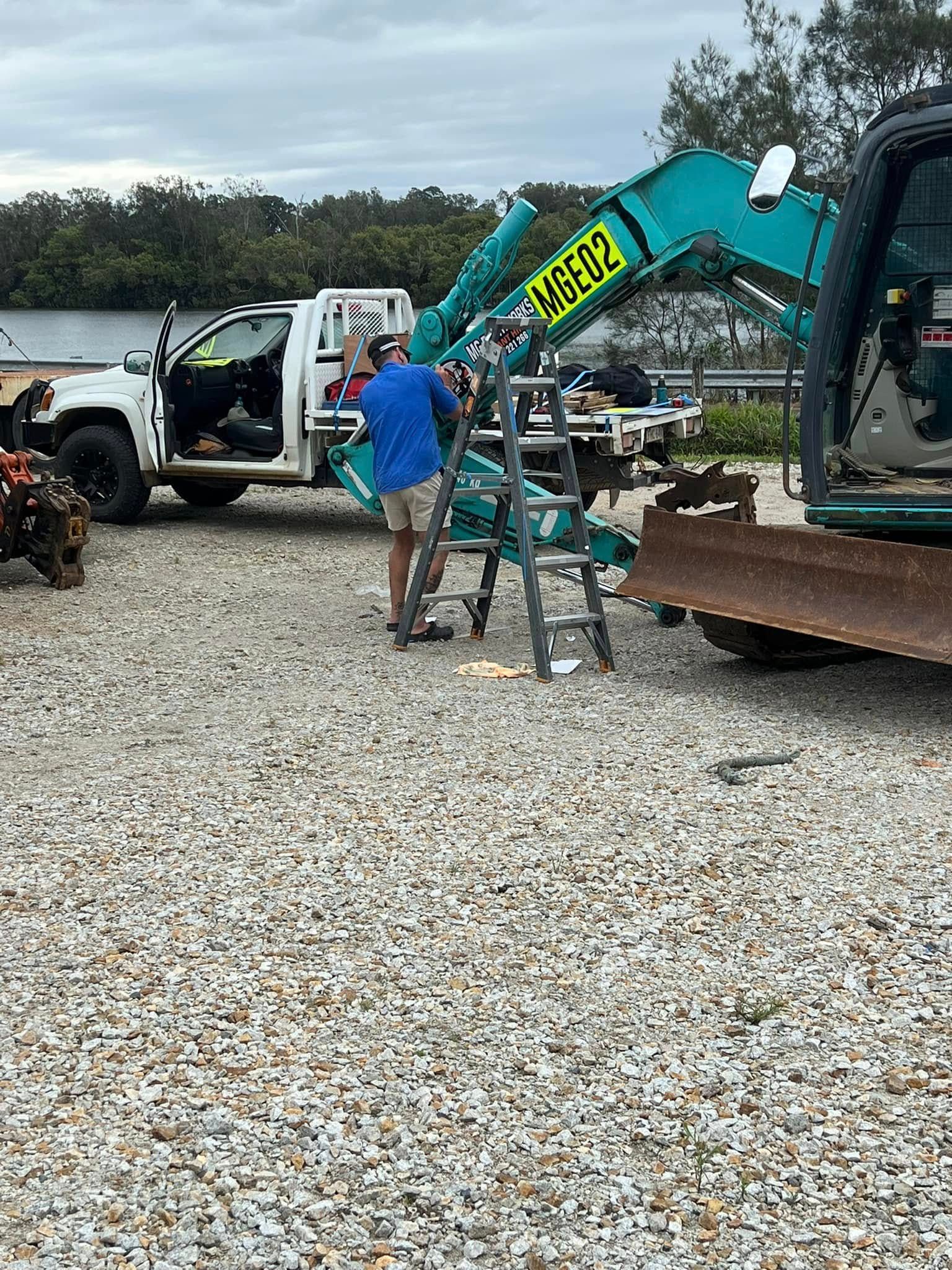 Man Repairs a Teal Excavator With a White Truck — MG Earthworks and Plant Hire in Nambucca, NSW