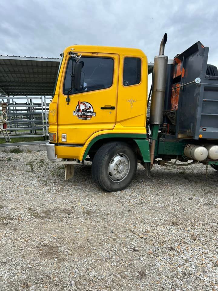 Yellow and green dump truck on gravel, cloudy sky.