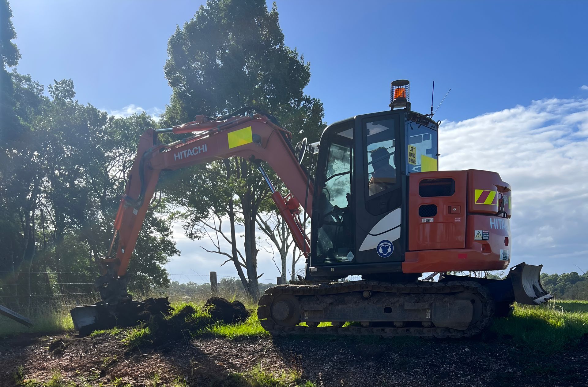 Orange Excavator Digging in Grassy Area — MG Earthworks and Plant Hire in Gumma, NSW