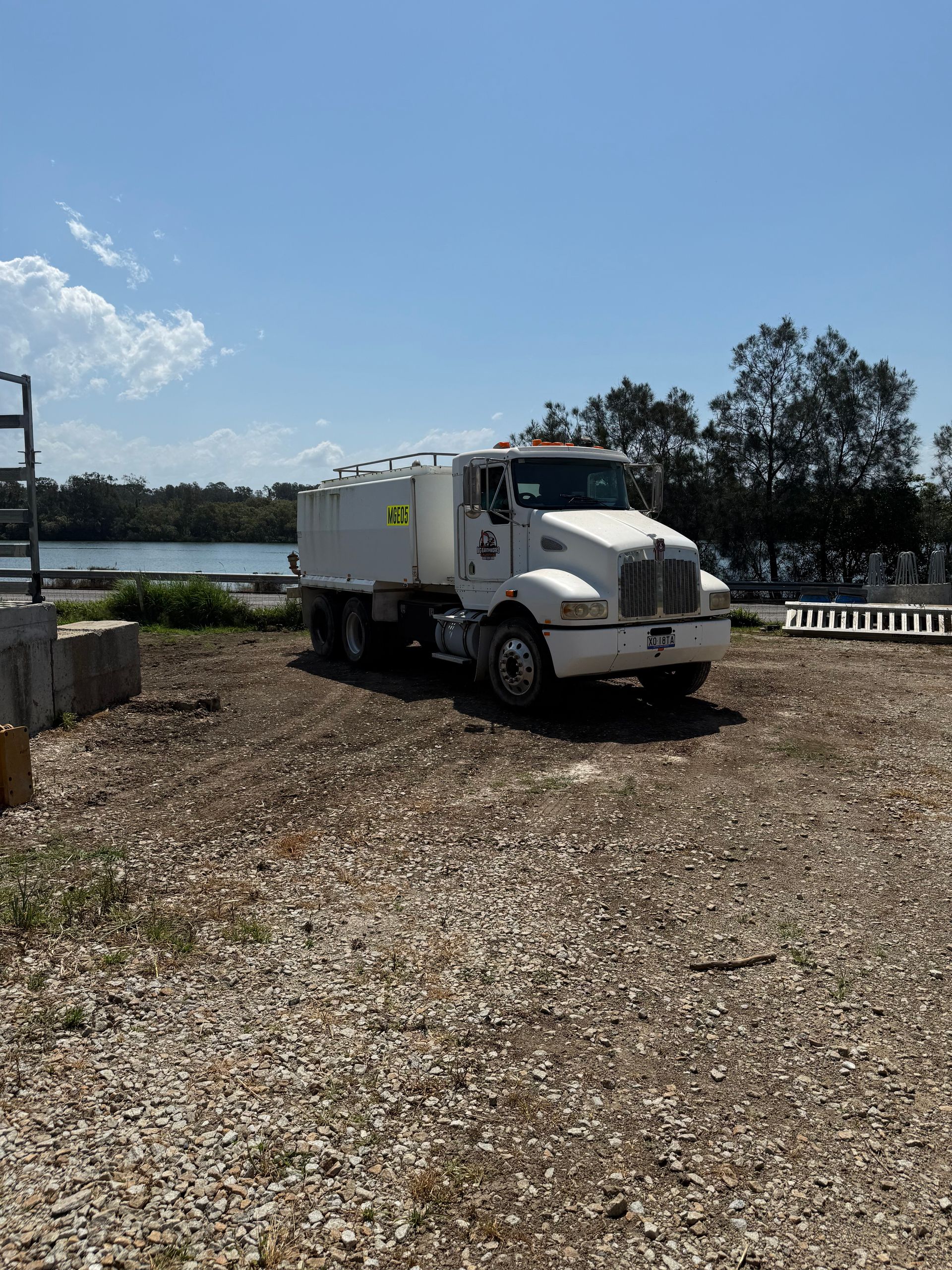 White water truck parked on gravel, near water and trees under a blue sky.