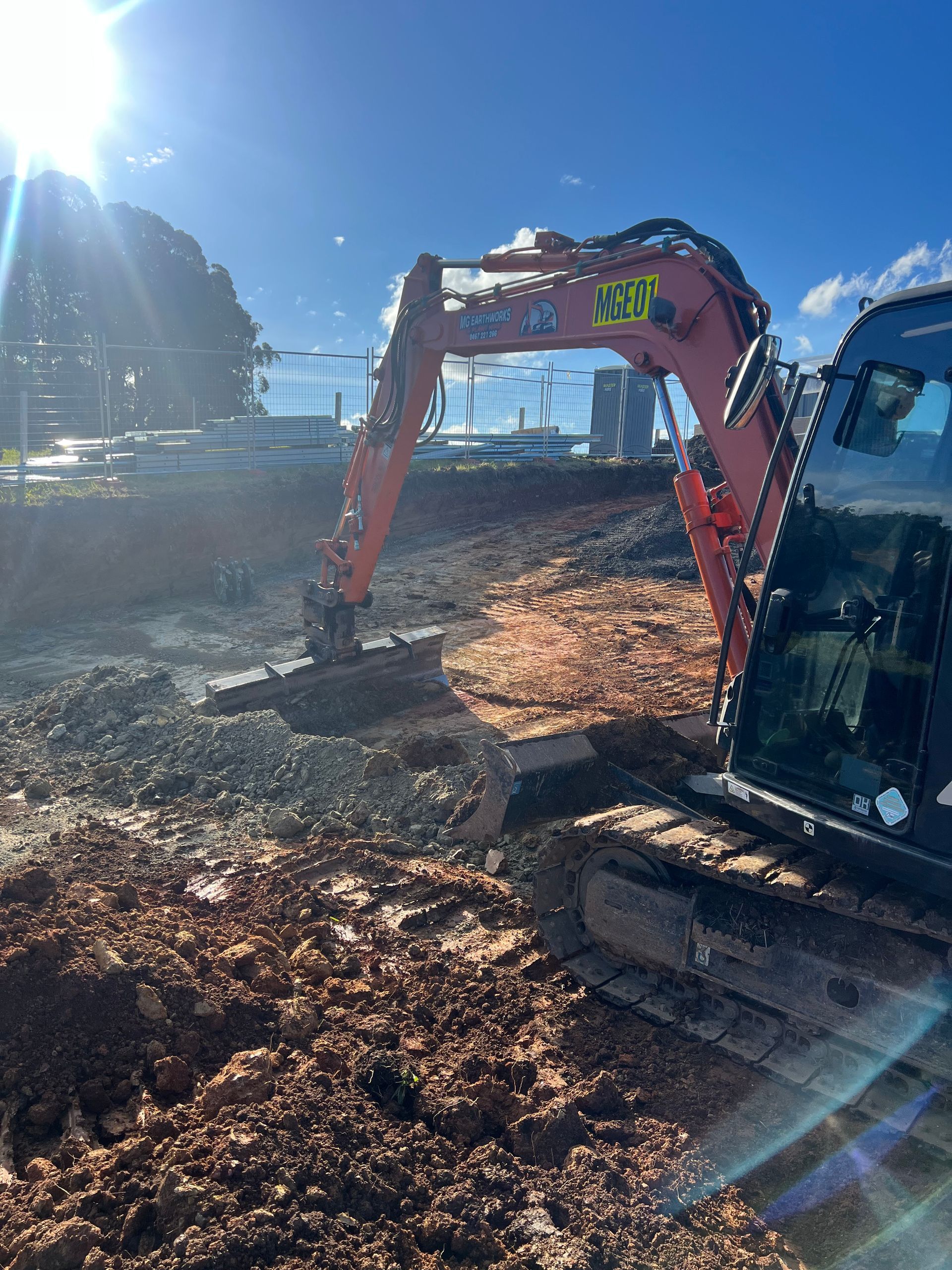 Red excavator digging in dirt on a construction site; sunny, daytime.