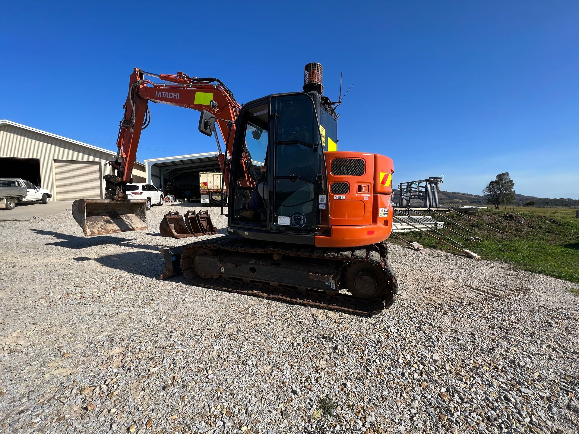 Orange excavator on gravel, with bucket and additional attachments. Sunny outdoor setting.