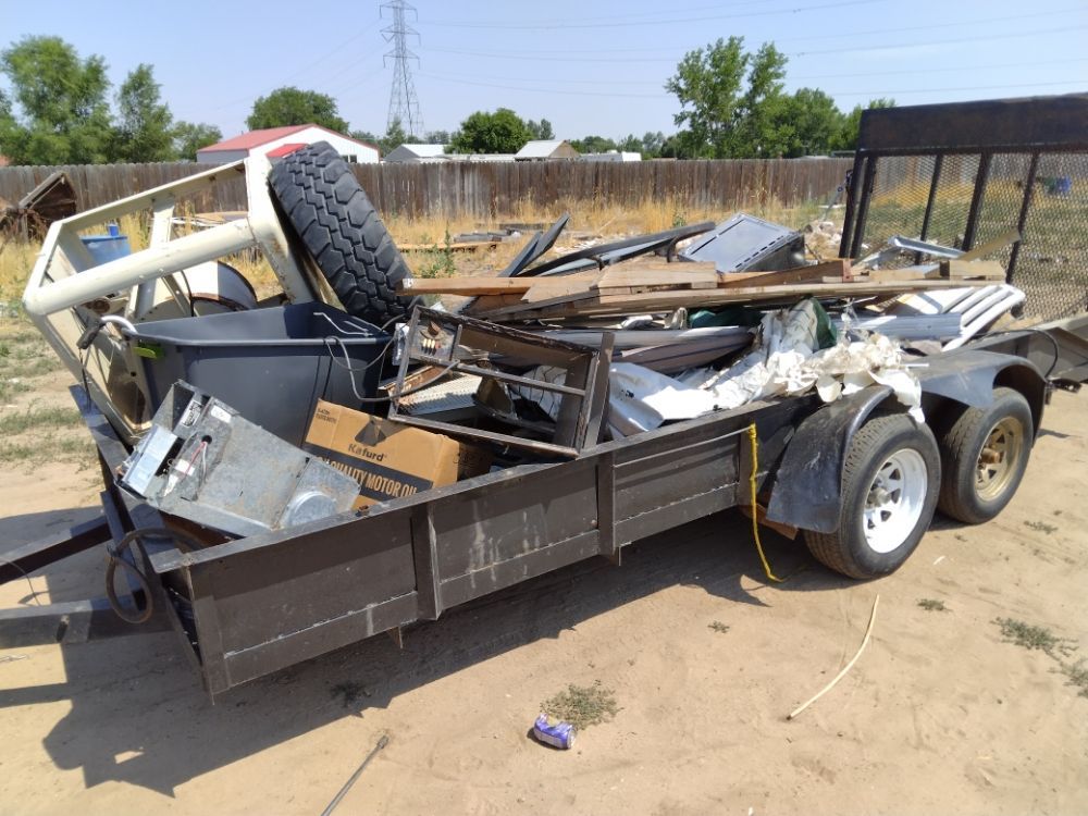 A trailer filled with junk is parked in a dirt field
