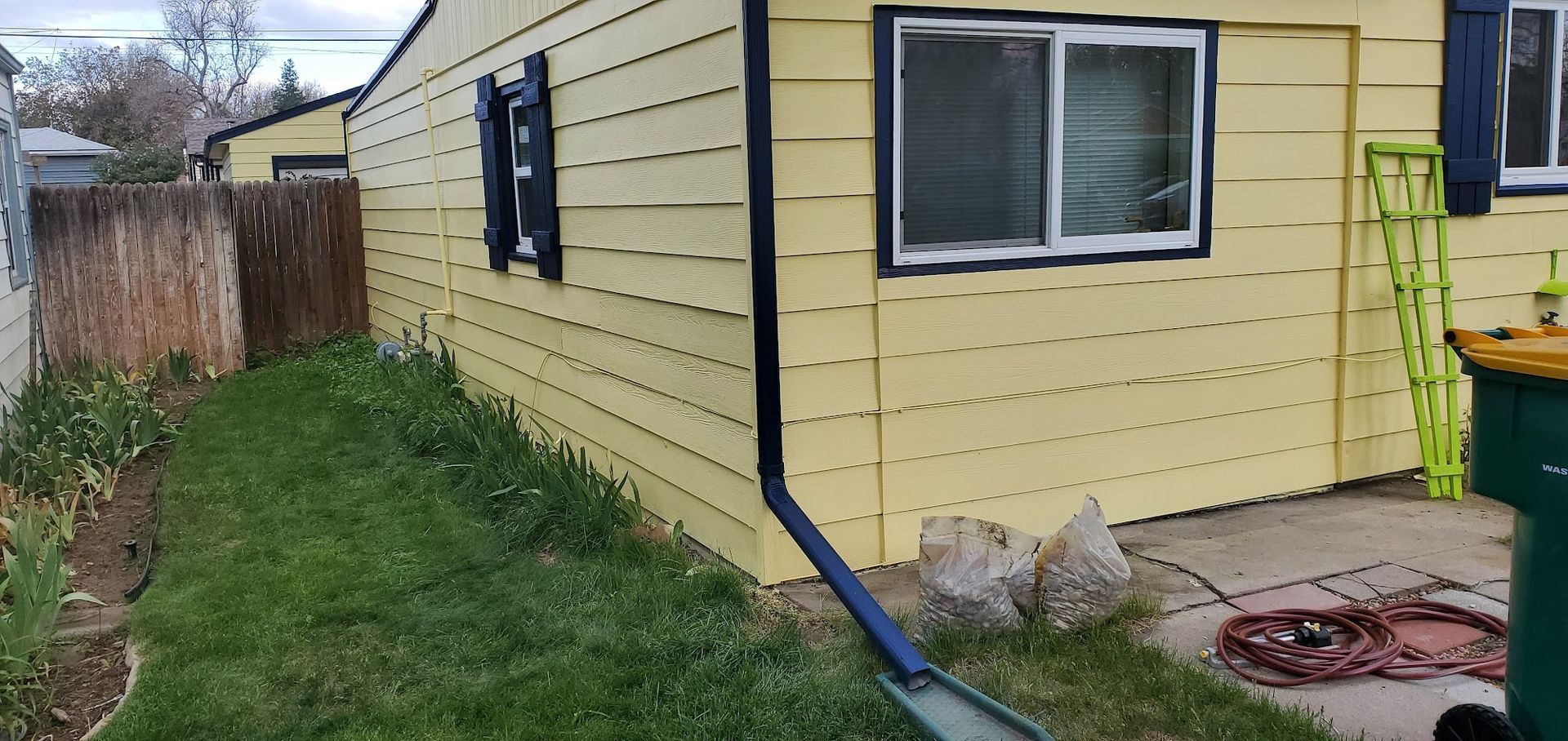 A yellow house with a green trash can in front of it.