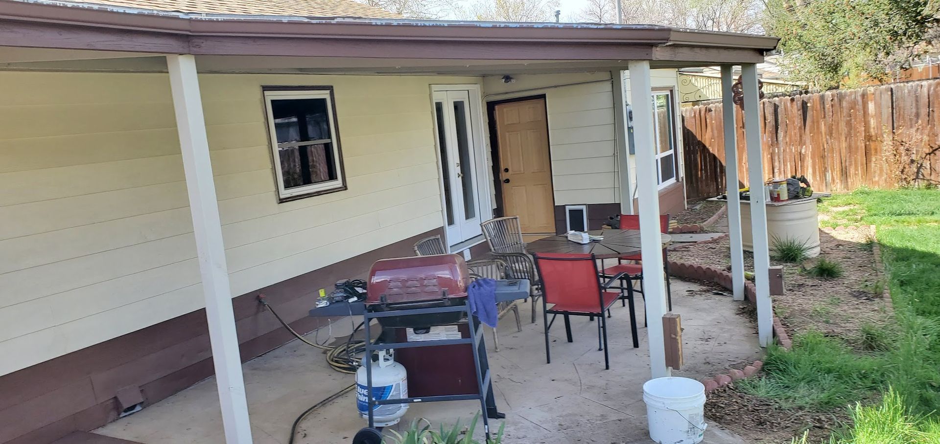 A patio with a grill and chairs in front of a house.