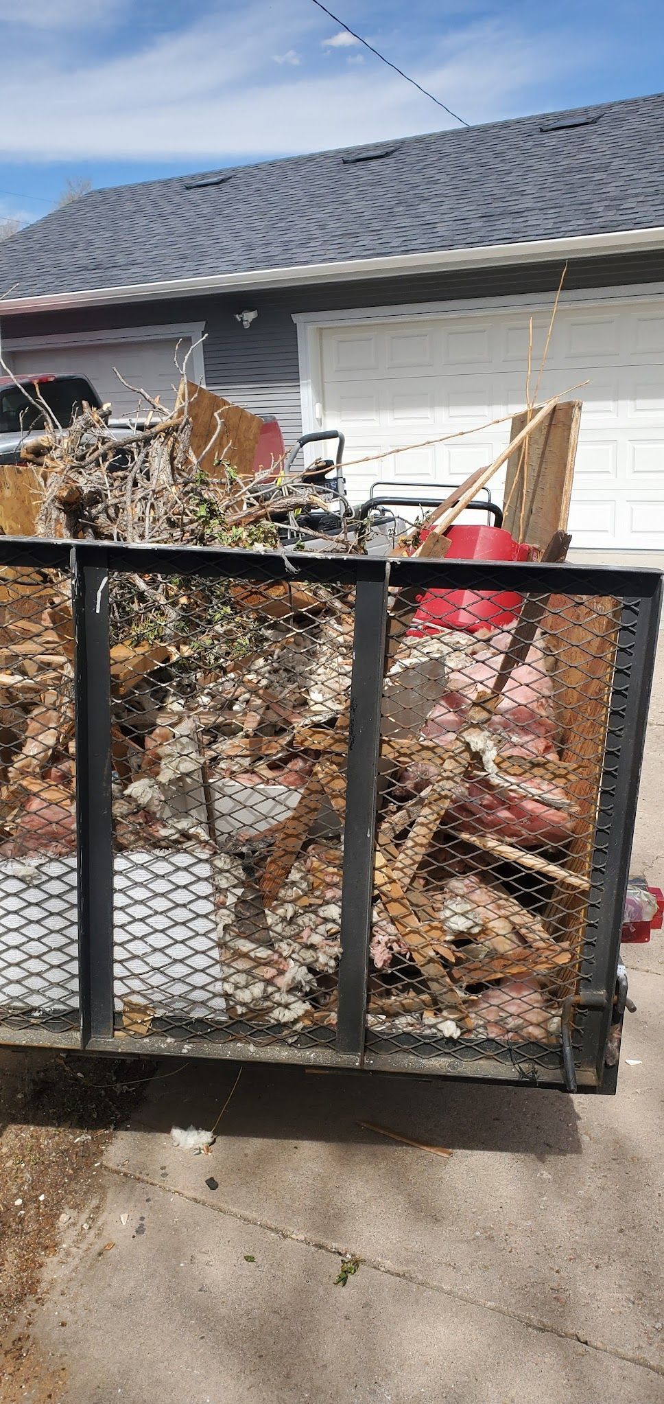 A dumpster filled with junk is parked in front of a house.