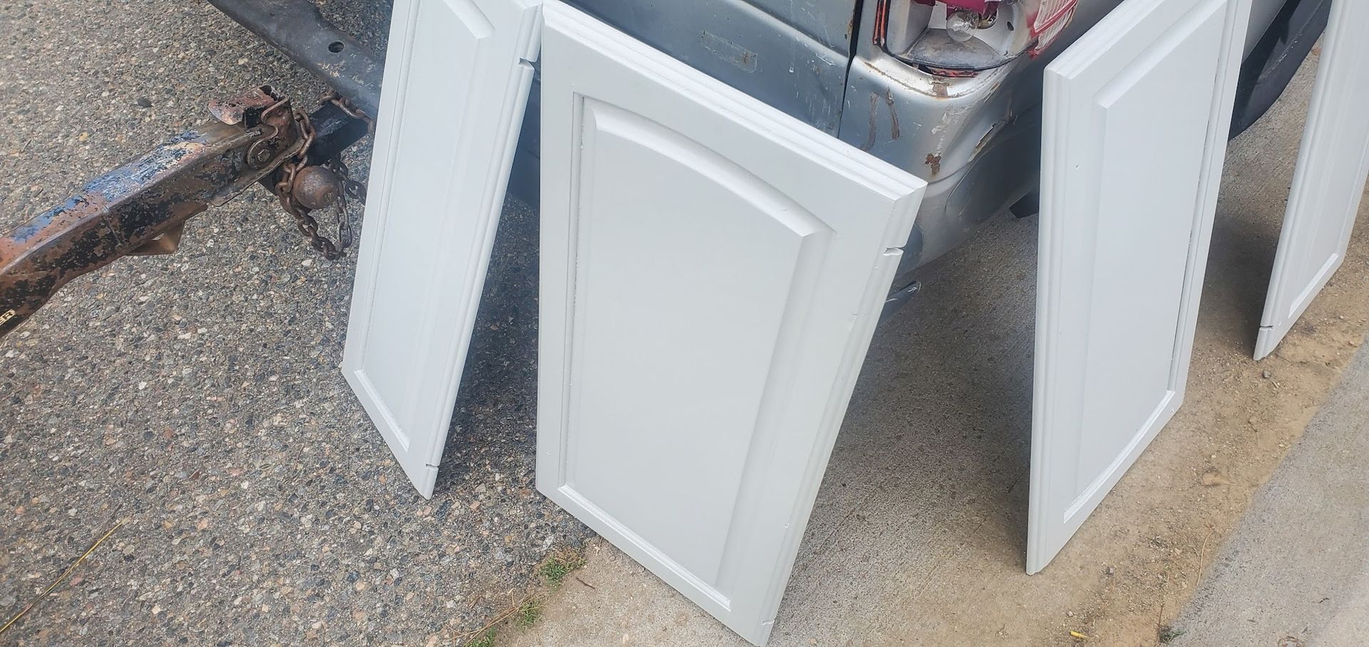 Three white cabinet doors are sitting on the ground next to a truck.