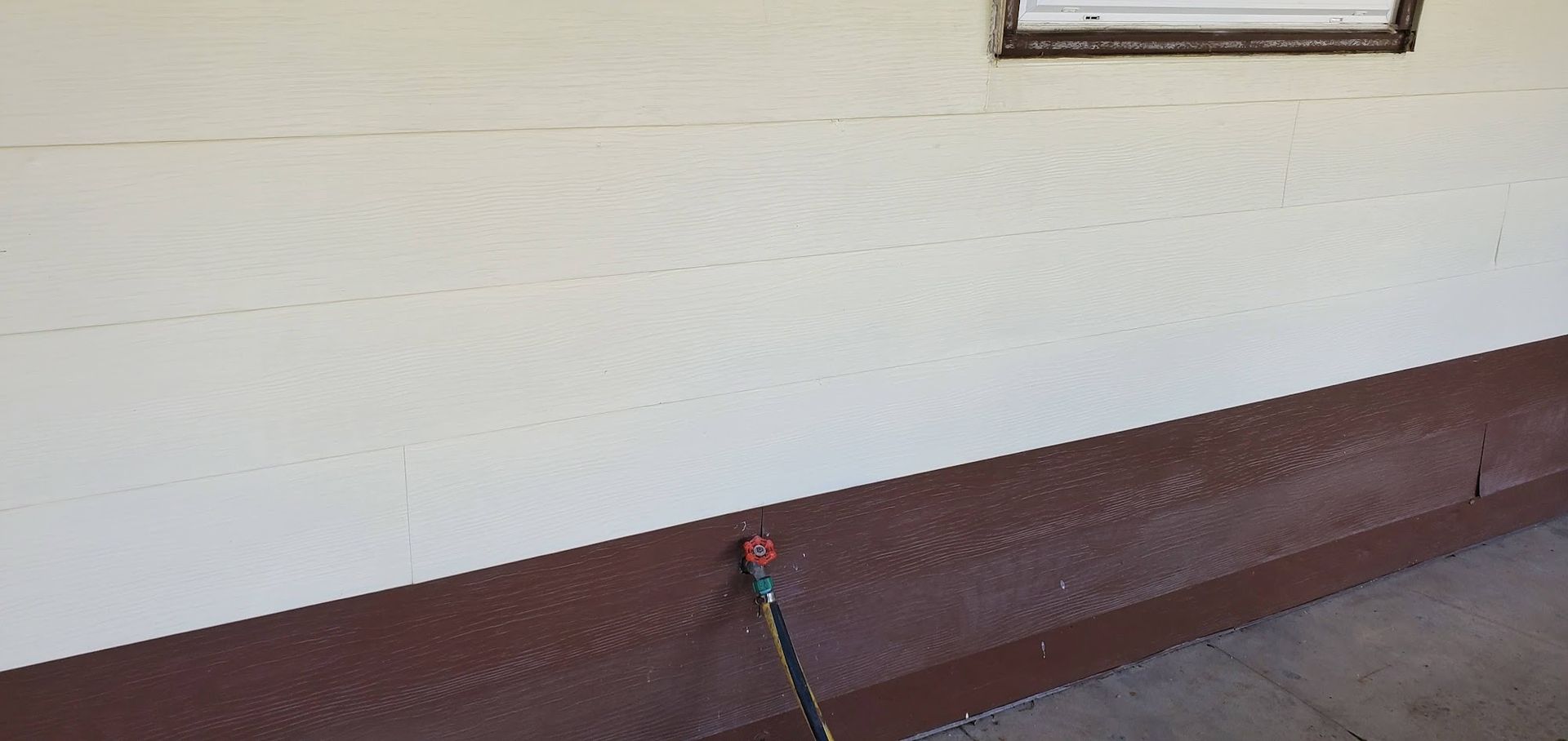 A hose is attached to the side of a building next to a window.