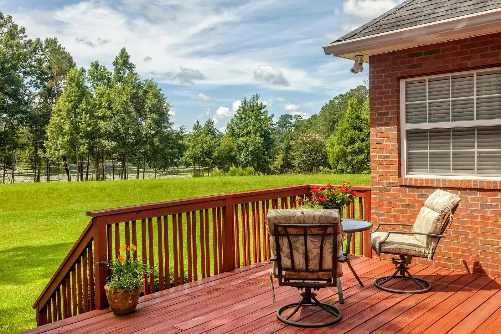 A wooden deck with chairs and a table in front of a brick house.