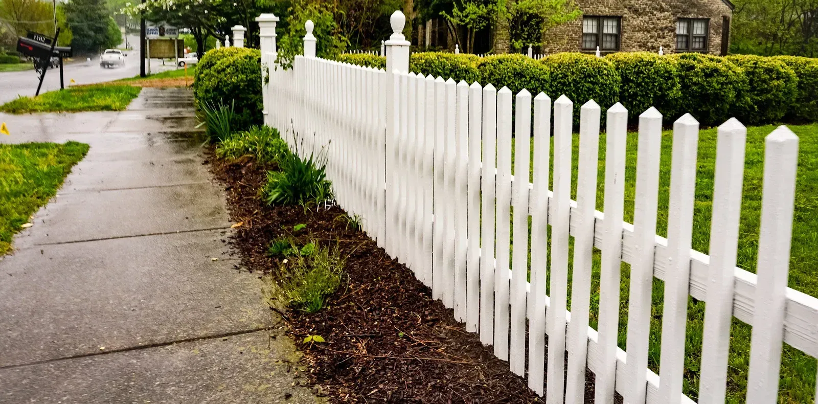 A white picket fence along a sidewalk next to a house.