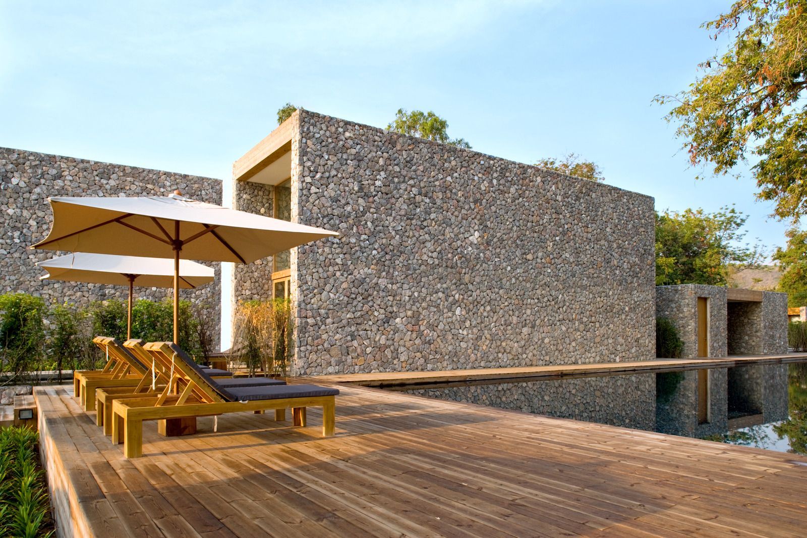 A wooden deck with chairs and umbrellas in front of a stone building