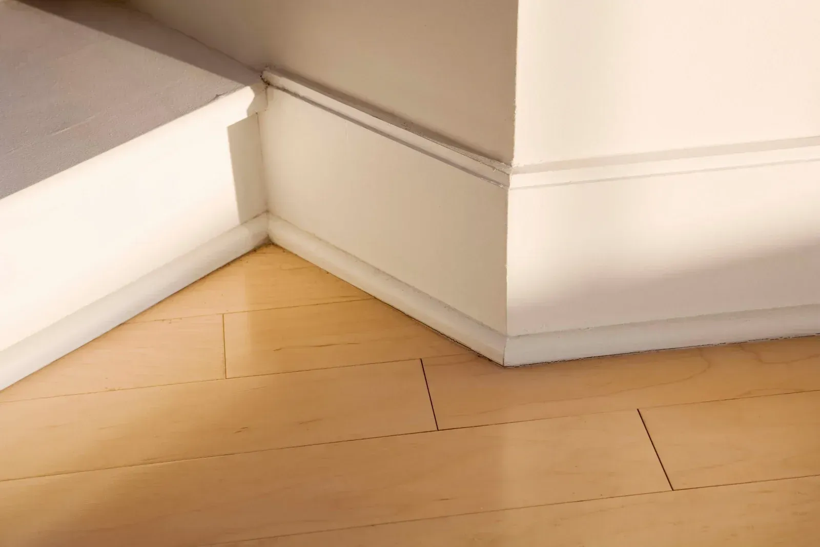A corner of a room with a wooden floor and white molding.