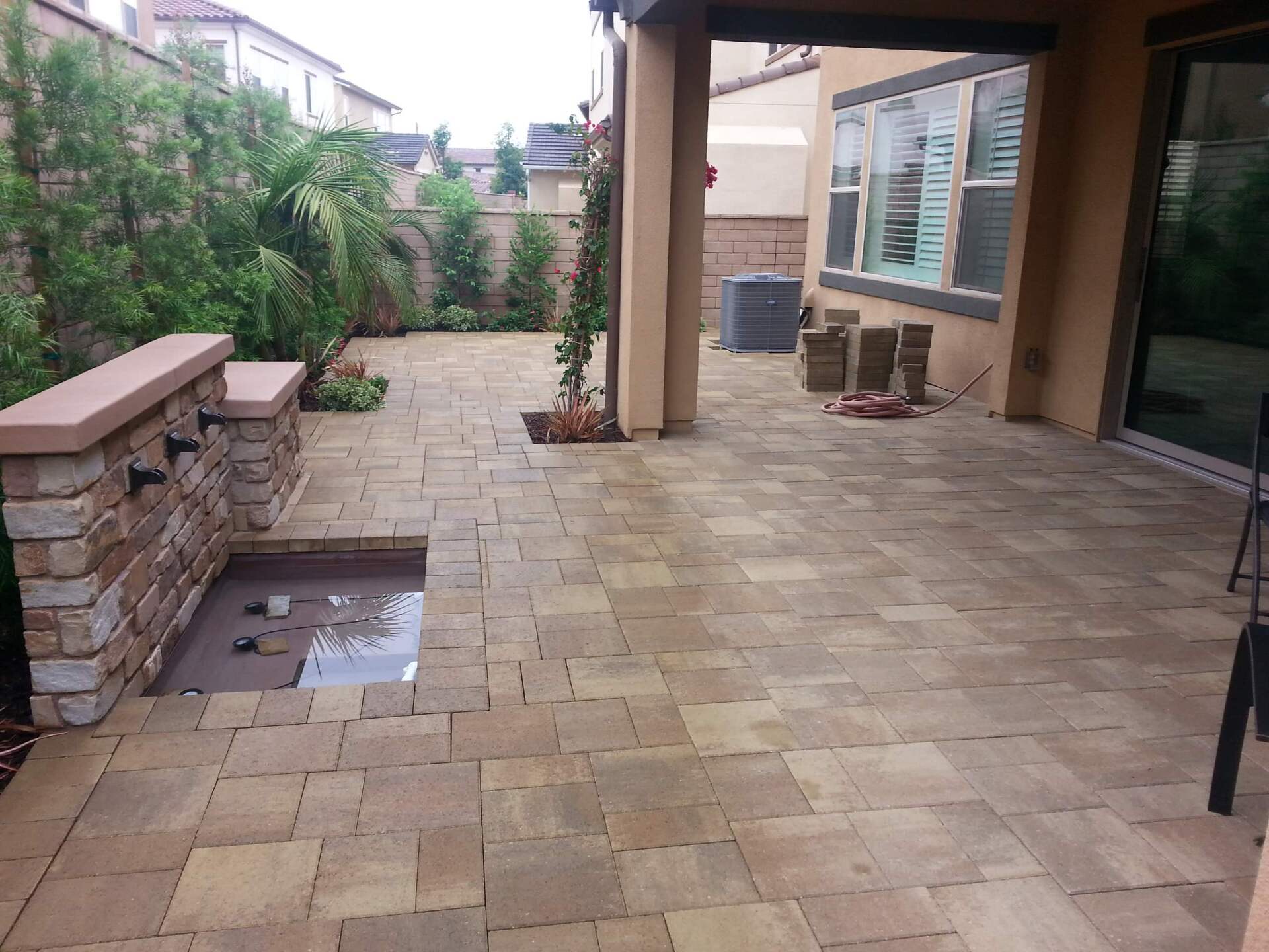 Patio with light-colored brick pavers, a stone wall, and a water feature.