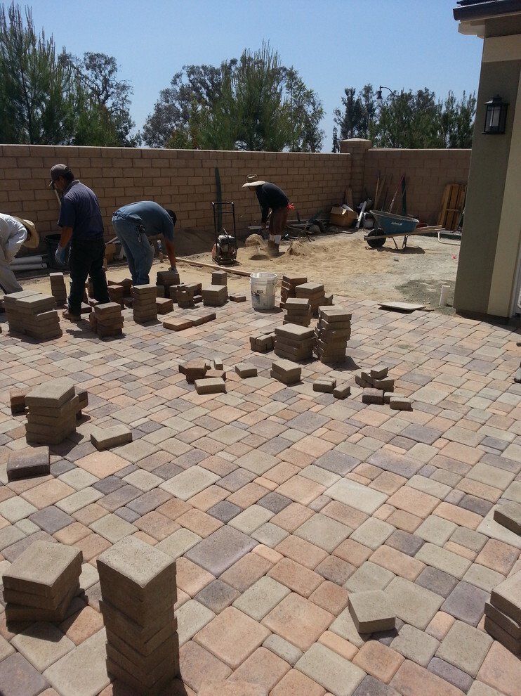 Workers laying paving stones in a backyard, sorting, and stacking bricks. Sunny day.