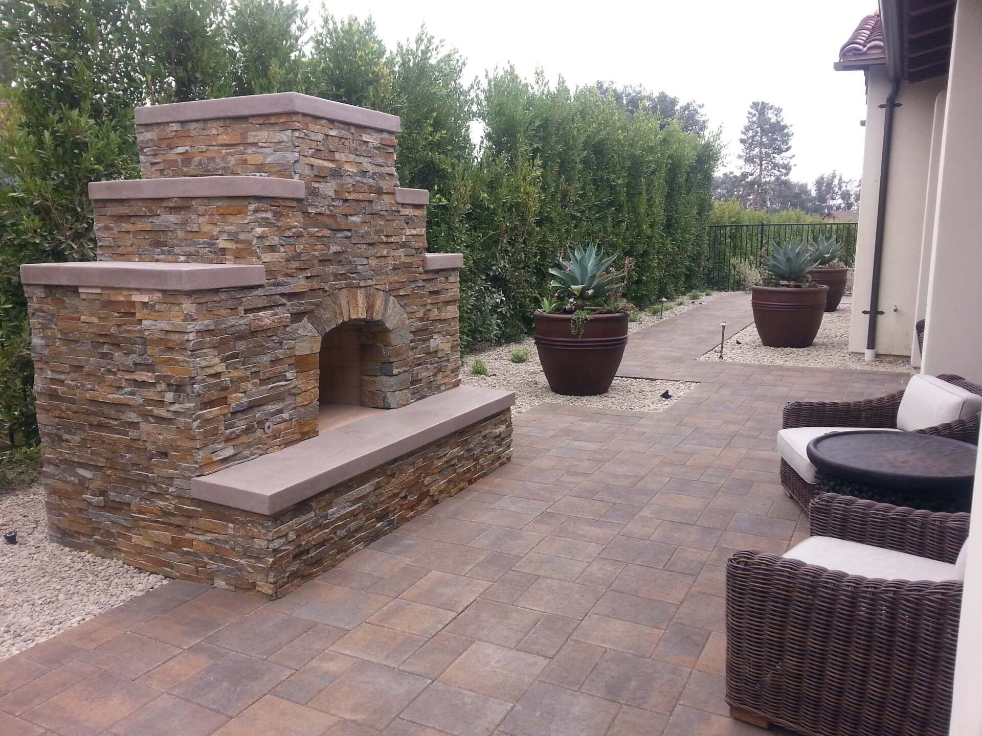 Stone fireplace and patio with seating, large planters, and greenery.