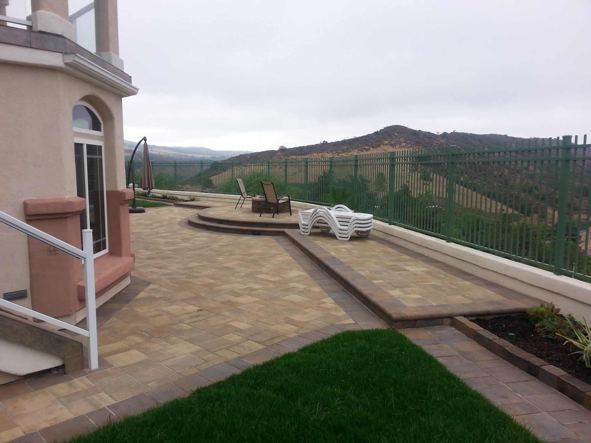 Patio with pavers, lounge chairs, fire pit, and a view of a mountain behind a fence.