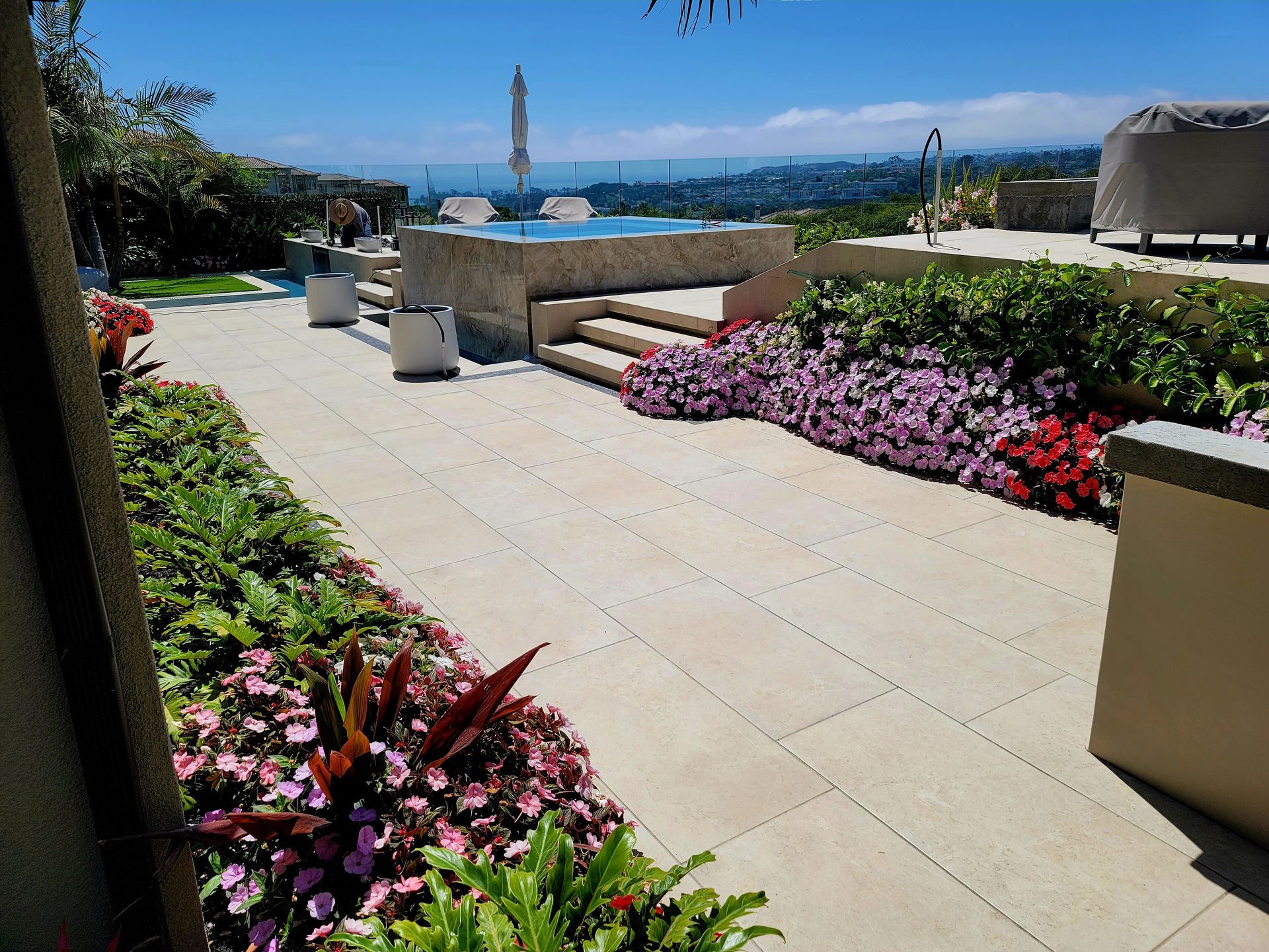 Patio with flowers, steps to a jacuzzi, overlooking ocean. Sunny day.