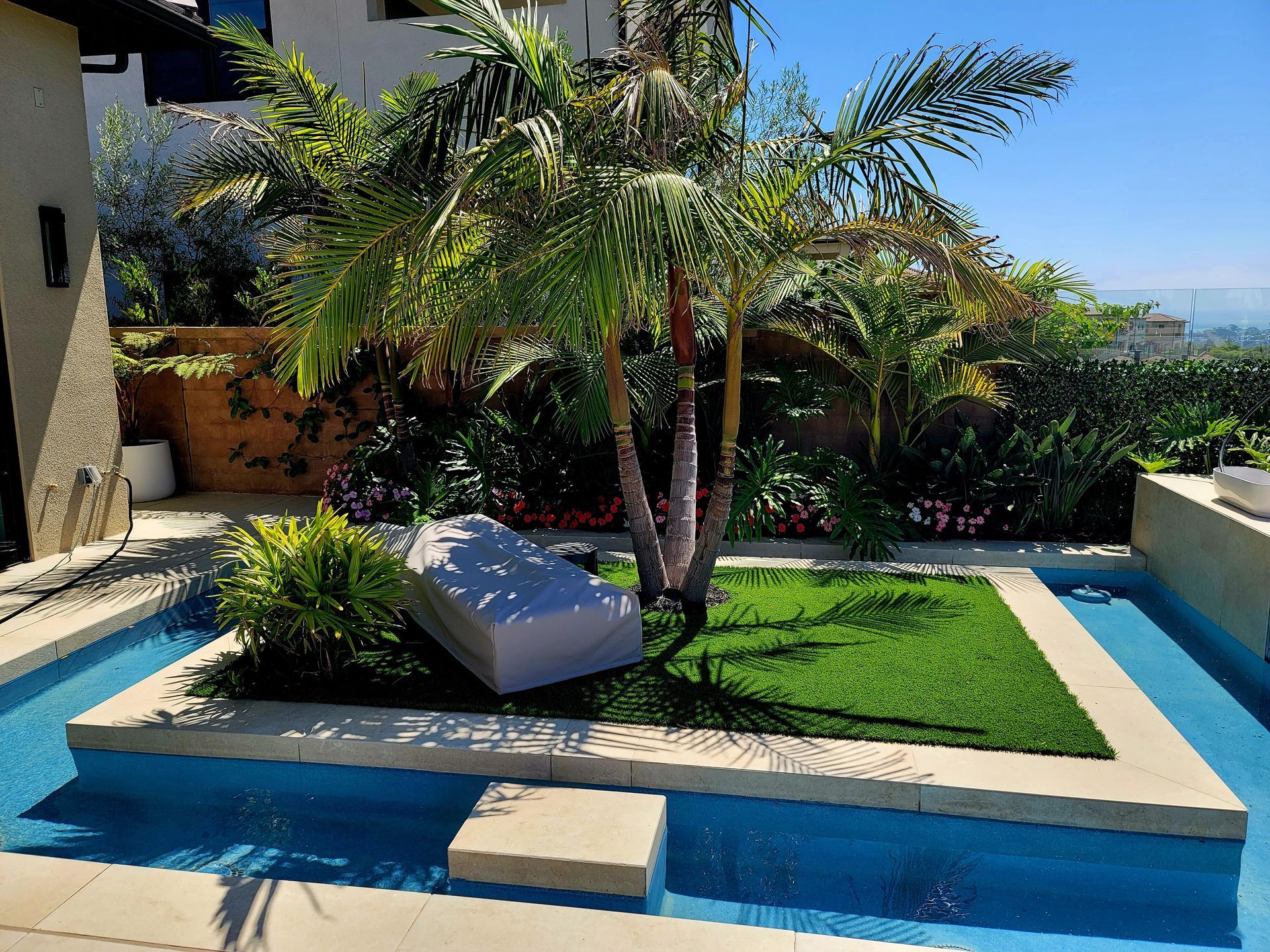 A small island with palm trees and artificial grass in a pool, next to a building.