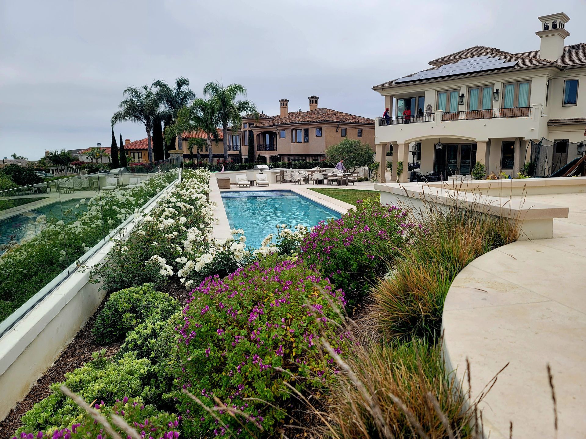 Luxury homes with a pool, gardens, and a coastal view on a cloudy day.