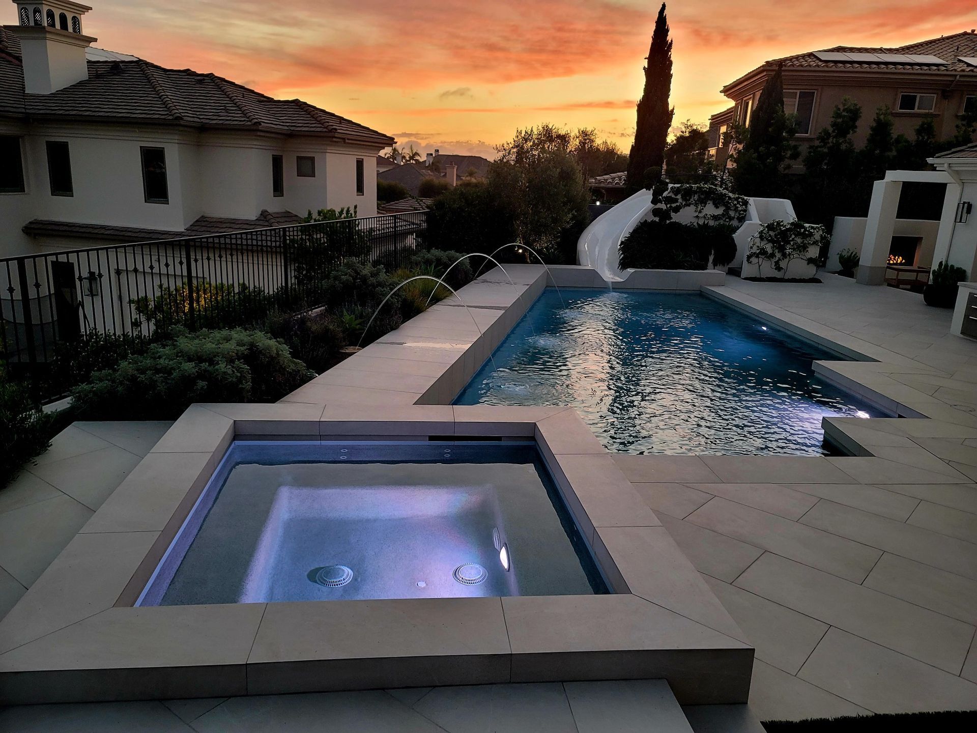 Pool and hot tub at dusk with a colorful sunset over luxury homes.