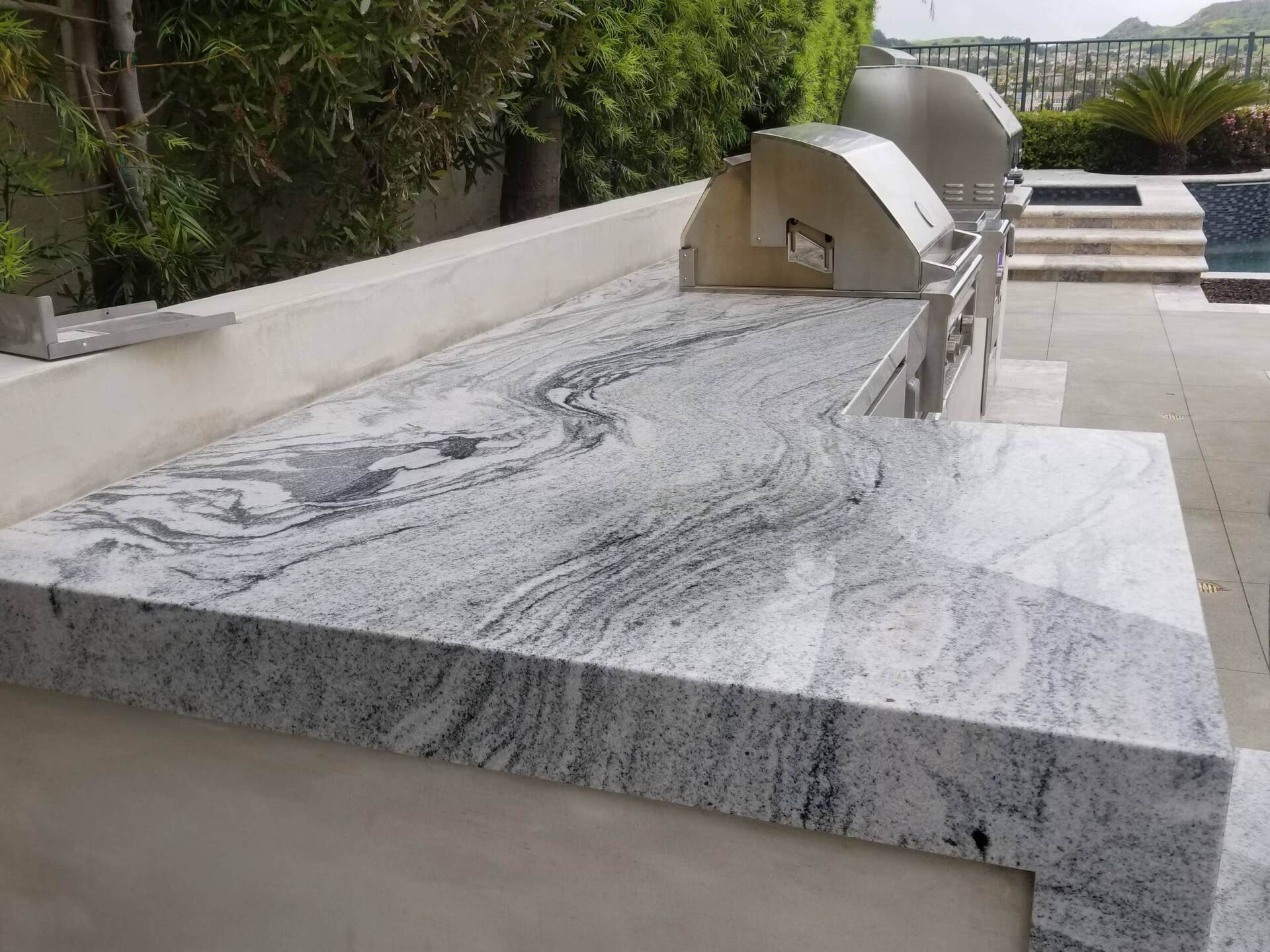 Outdoor granite countertop with built-in grill, overlooking a pool.
