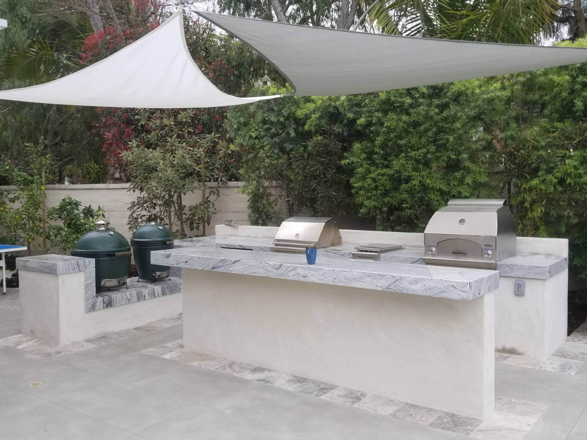 Outdoor kitchen with granite countertop, grills, and shade sail.