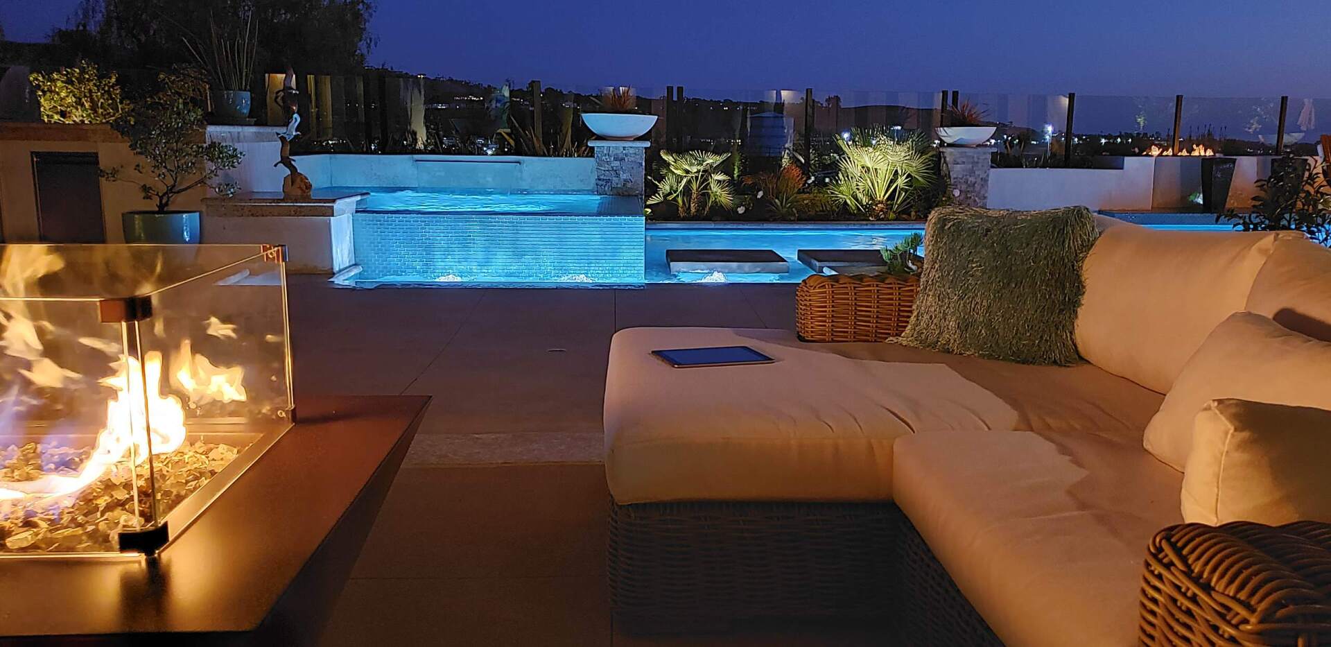 Rooftop patio at night with pool, fire pit, and lounge seating; blue and warm lighting.