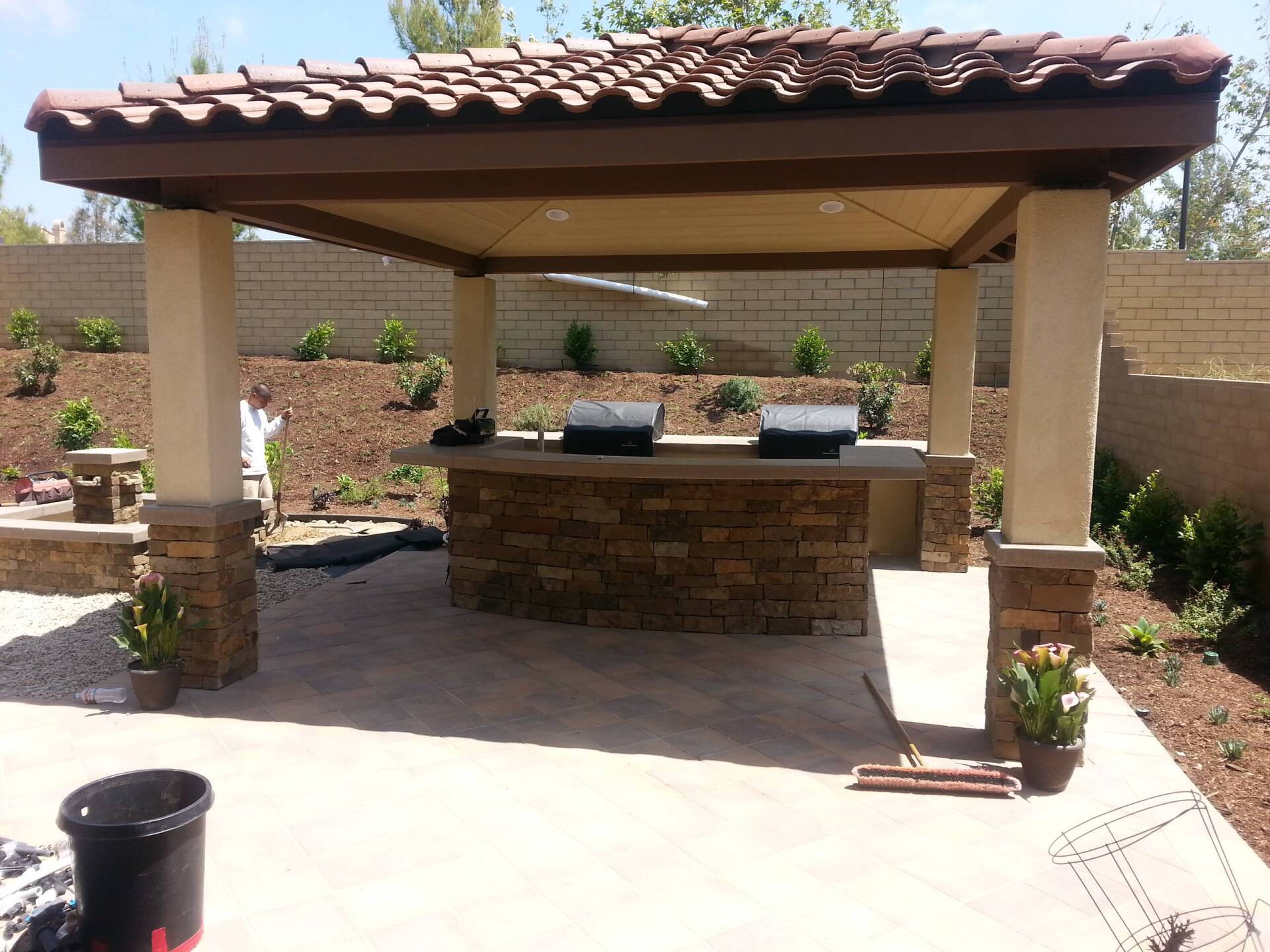 Outdoor kitchen with stone facade, tile roof, and built-in grills on a patio.