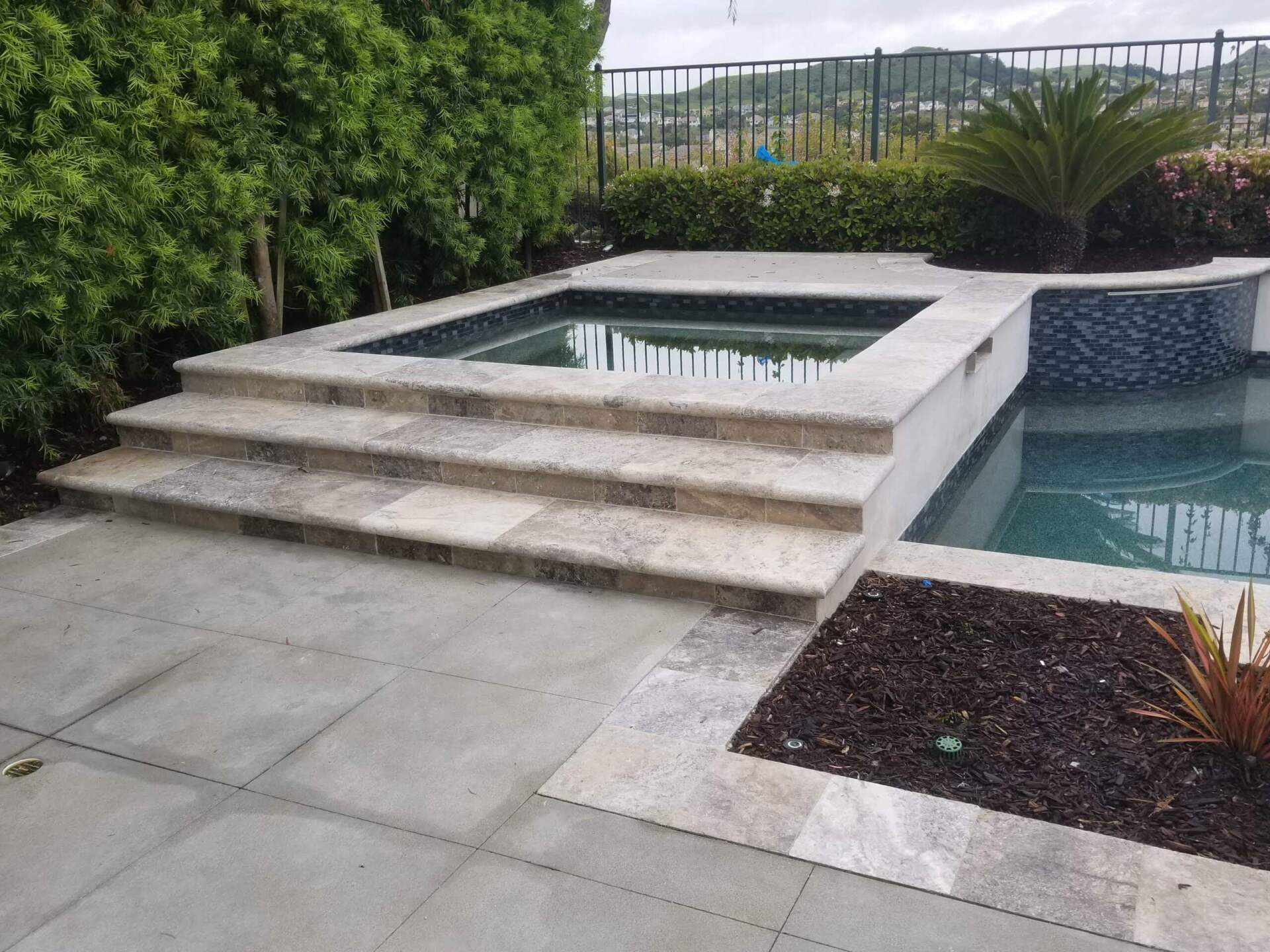 Stone steps leading to a spa next to a pool with lush greenery in the background.