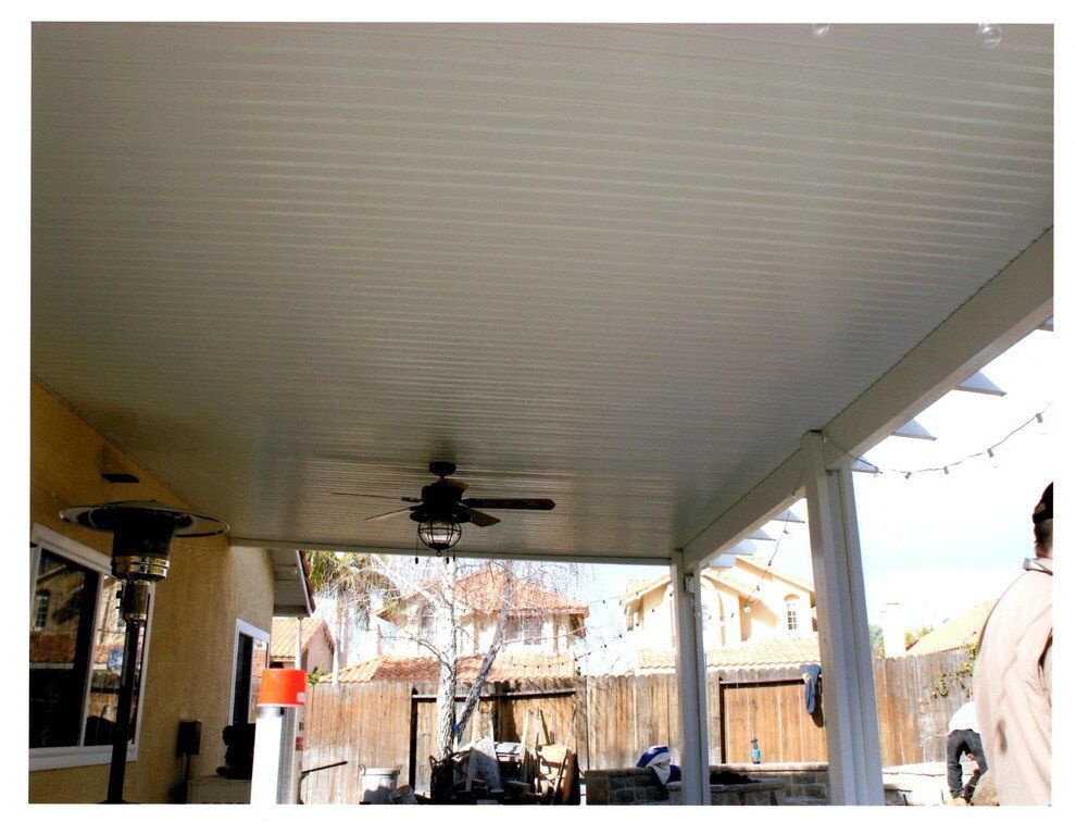 Patio roof with ceiling fan, white supports, and view of a residential backyard.