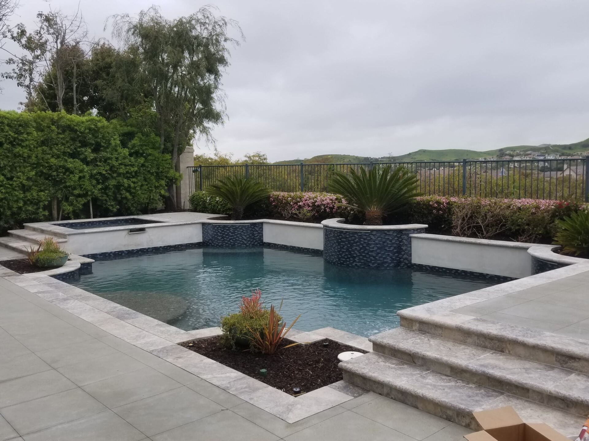 Pool with blue tile, spa, and landscaping on a cloudy day.