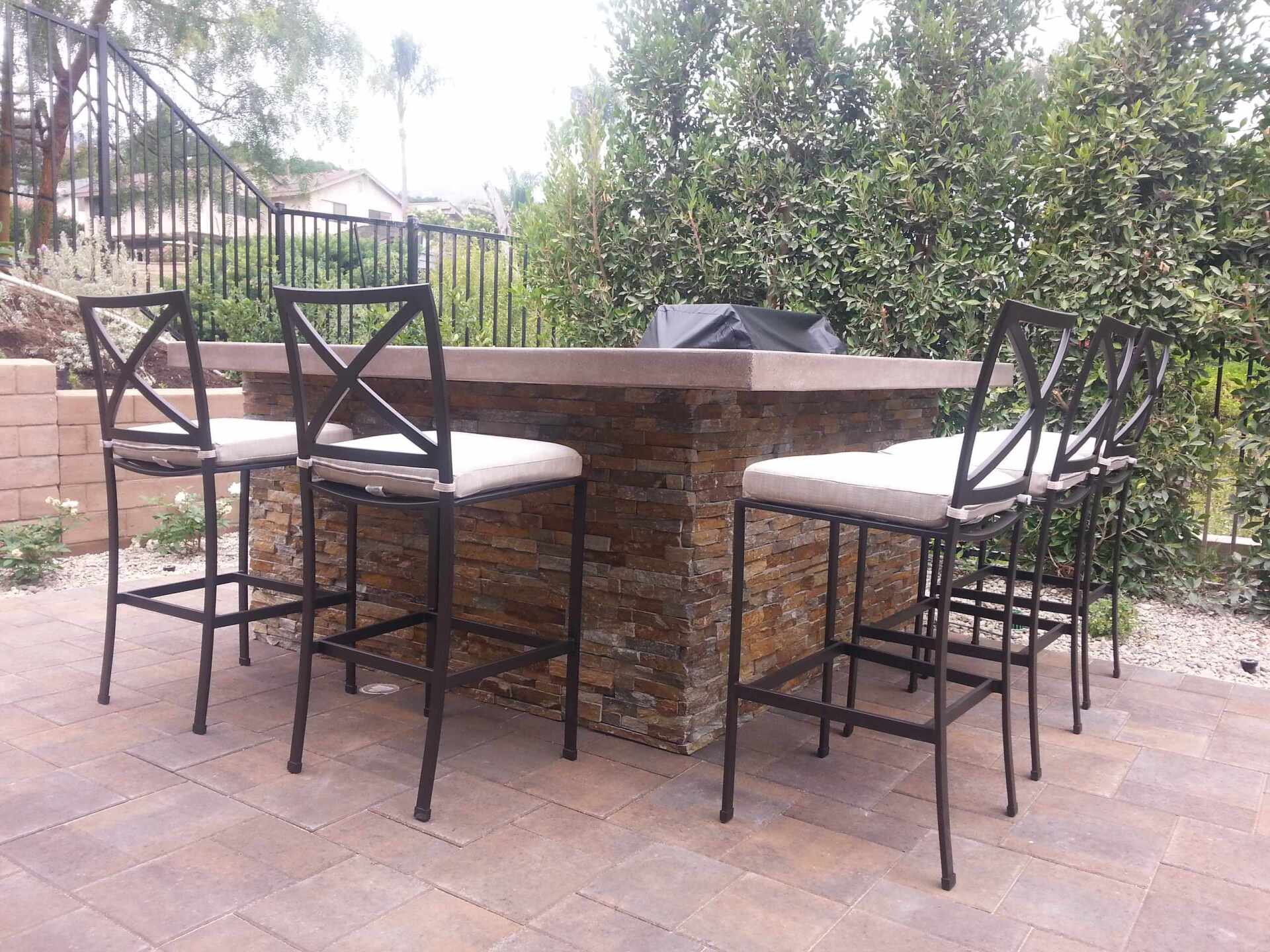 Outdoor bar with stone facade and metal chairs with cushions.