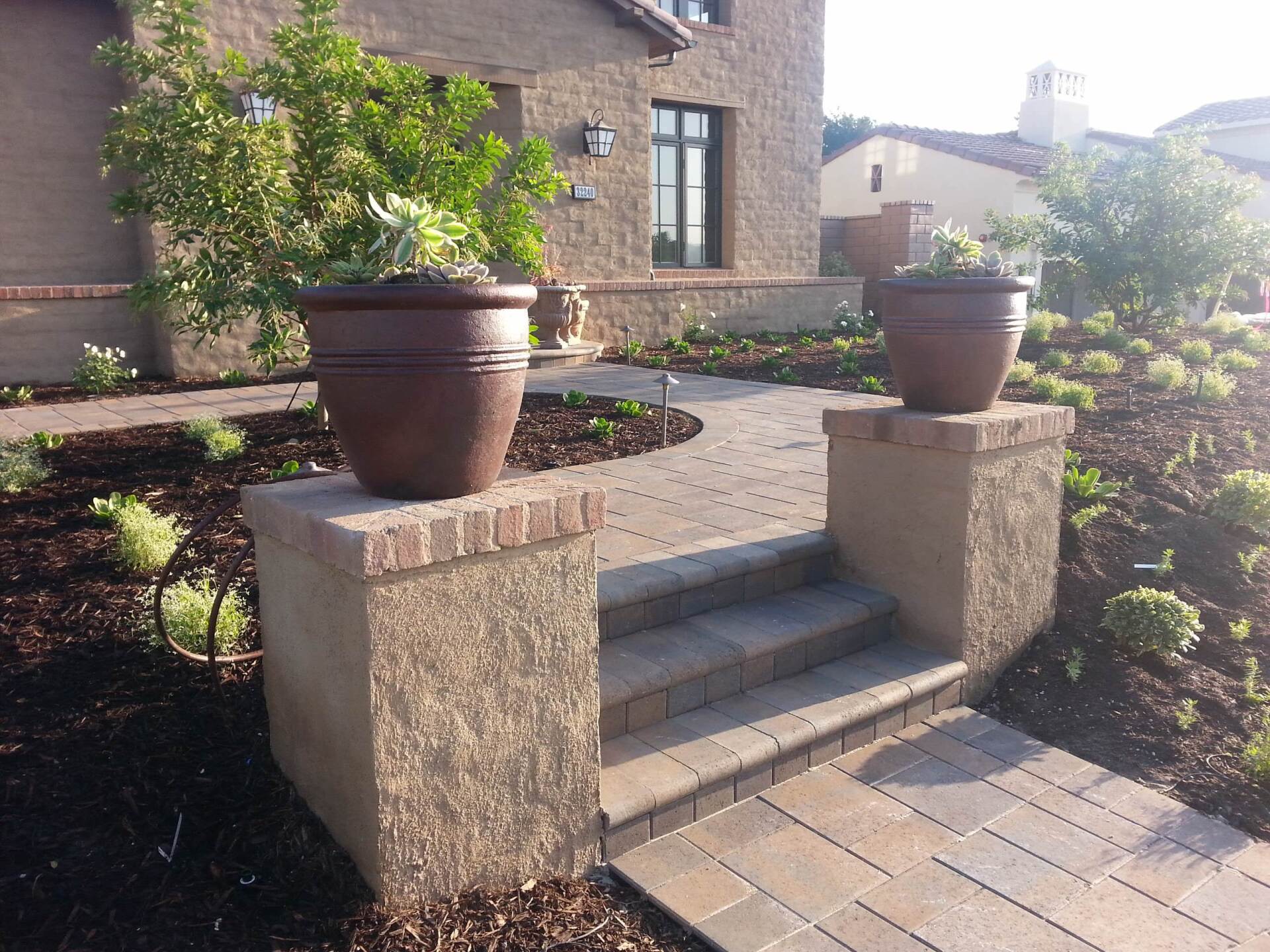 Brick walkway with stairs leading to a house entrance, flanked by planters with succulent plants.