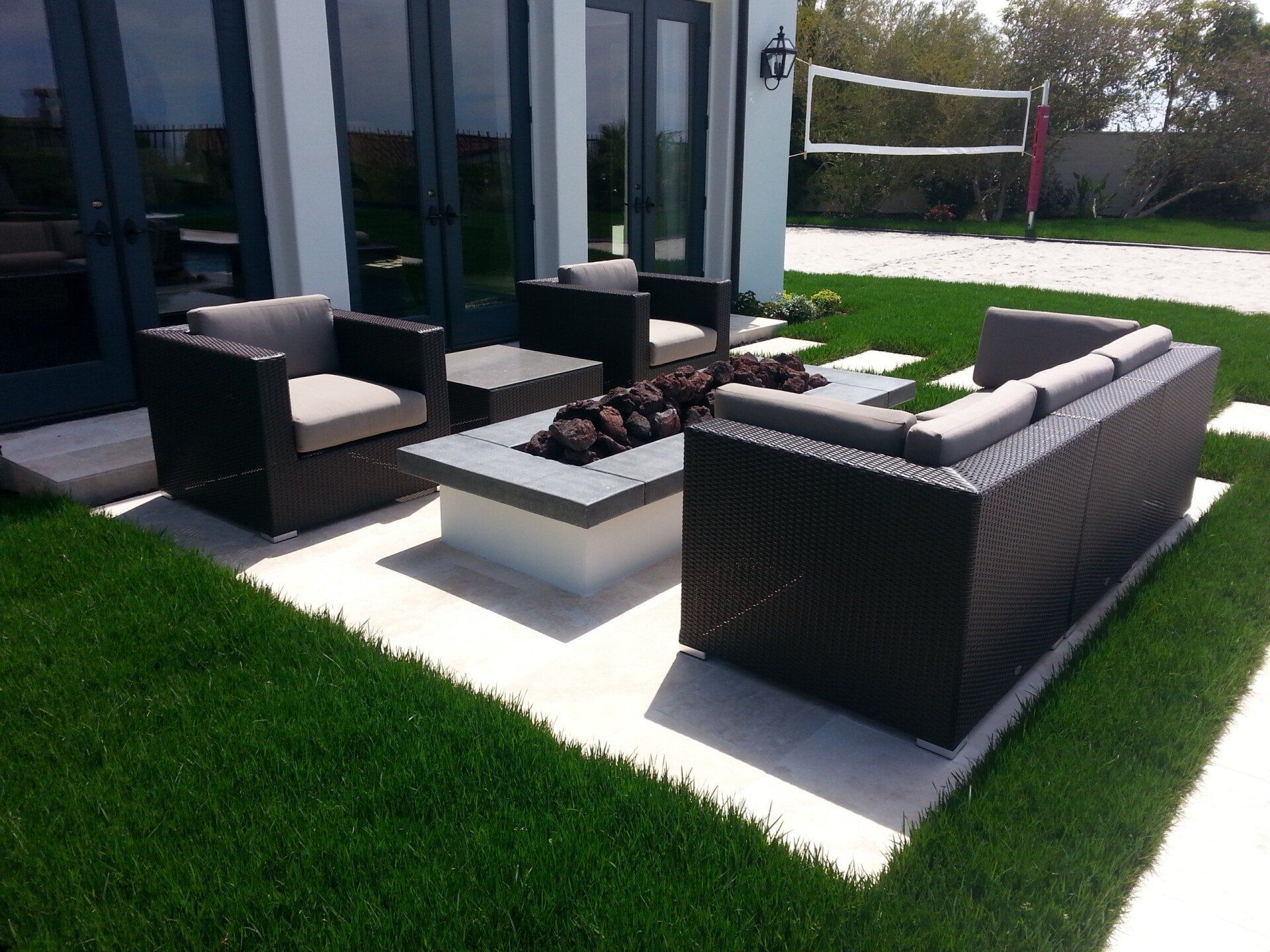 Outdoor seating area with black wicker furniture, fire pit, and volleyball net.