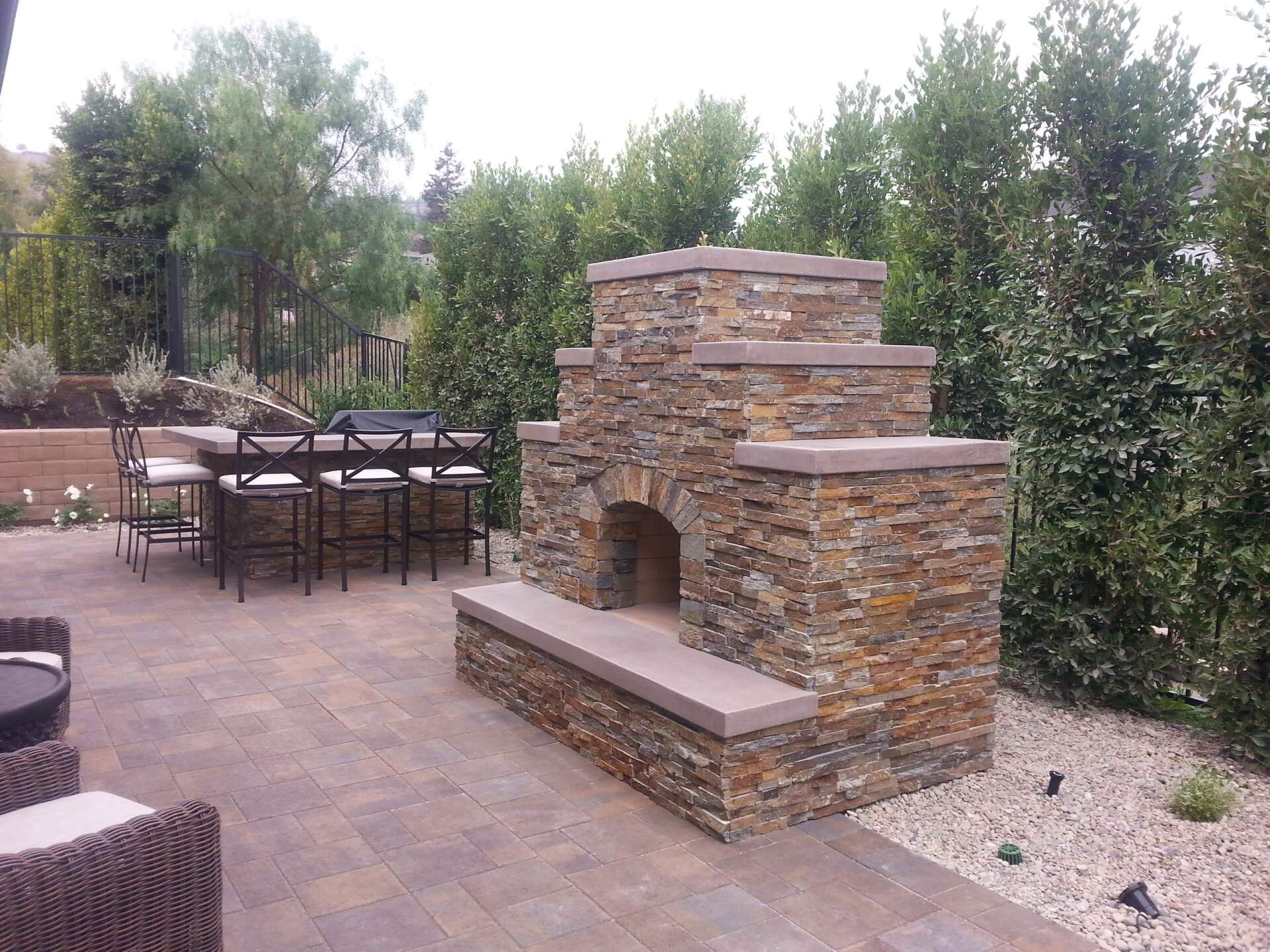 Outdoor patio with a stone fireplace, seating, and lush greenery.