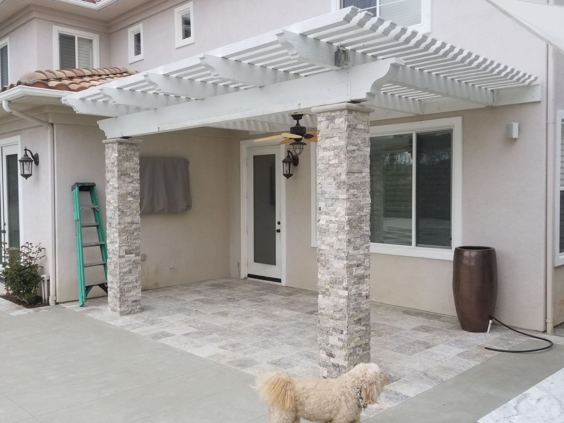 Pergola with stone columns and patterned patio, dog in foreground, house in background.
