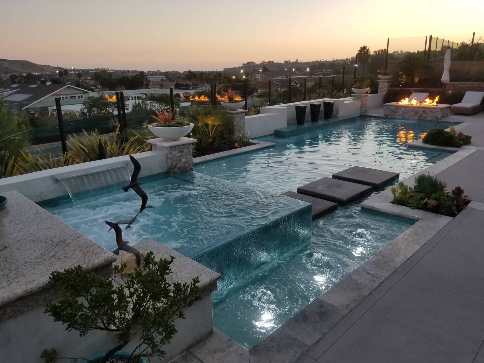 Luxury backyard pool with cascading water, fire pit, and city views at dusk.