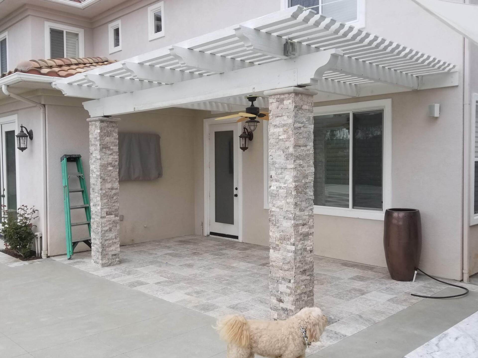Pergola-covered patio with stone columns, dog, and patterned stone floor.