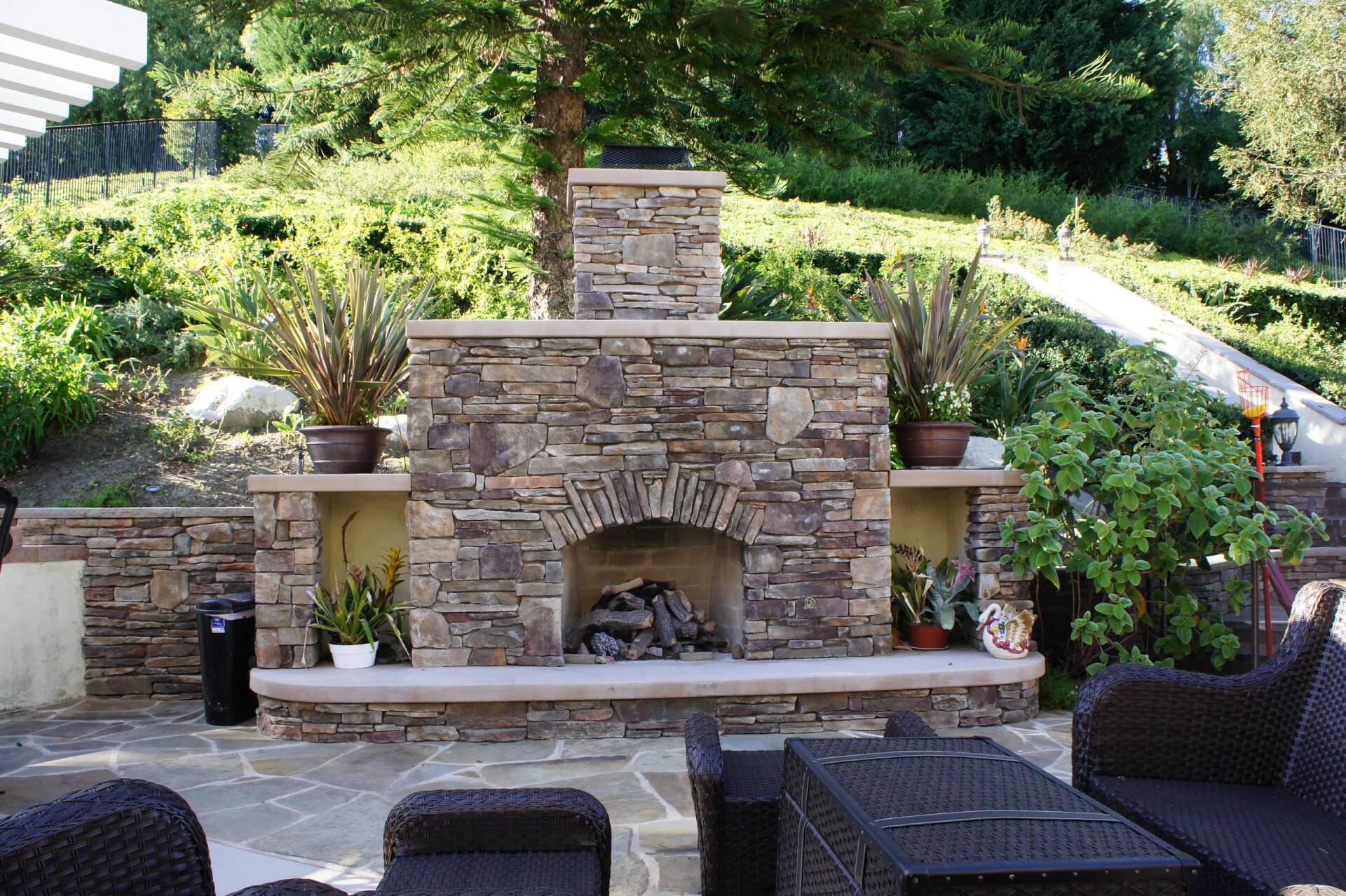 Stone fireplace in a backyard setting, with seating and surrounding greenery.