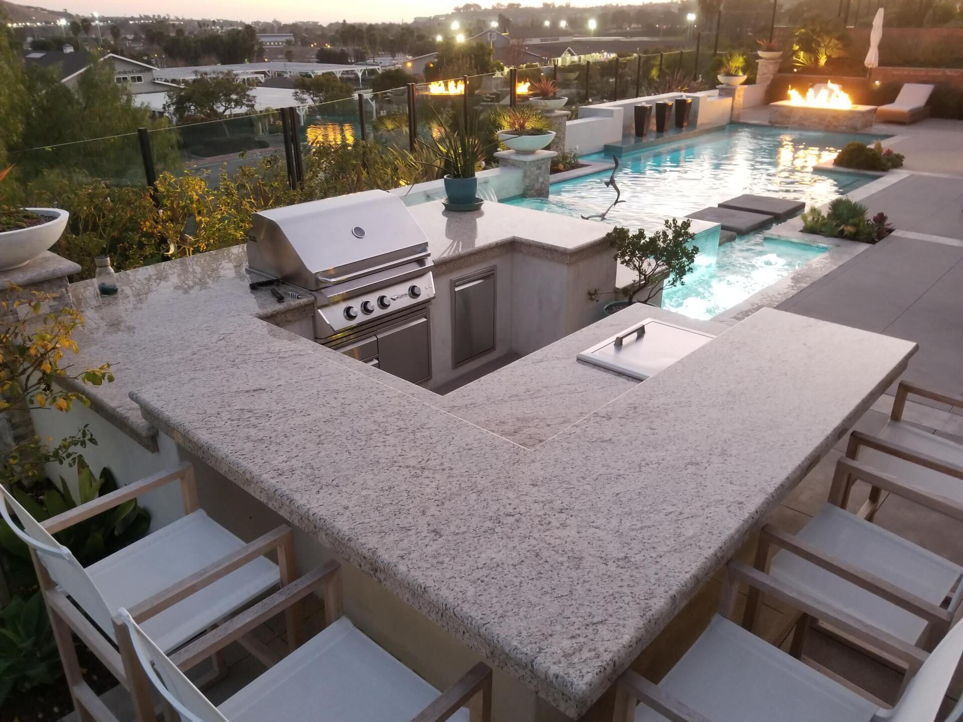 Outdoor kitchen with a grill, seating, and pool in the background.