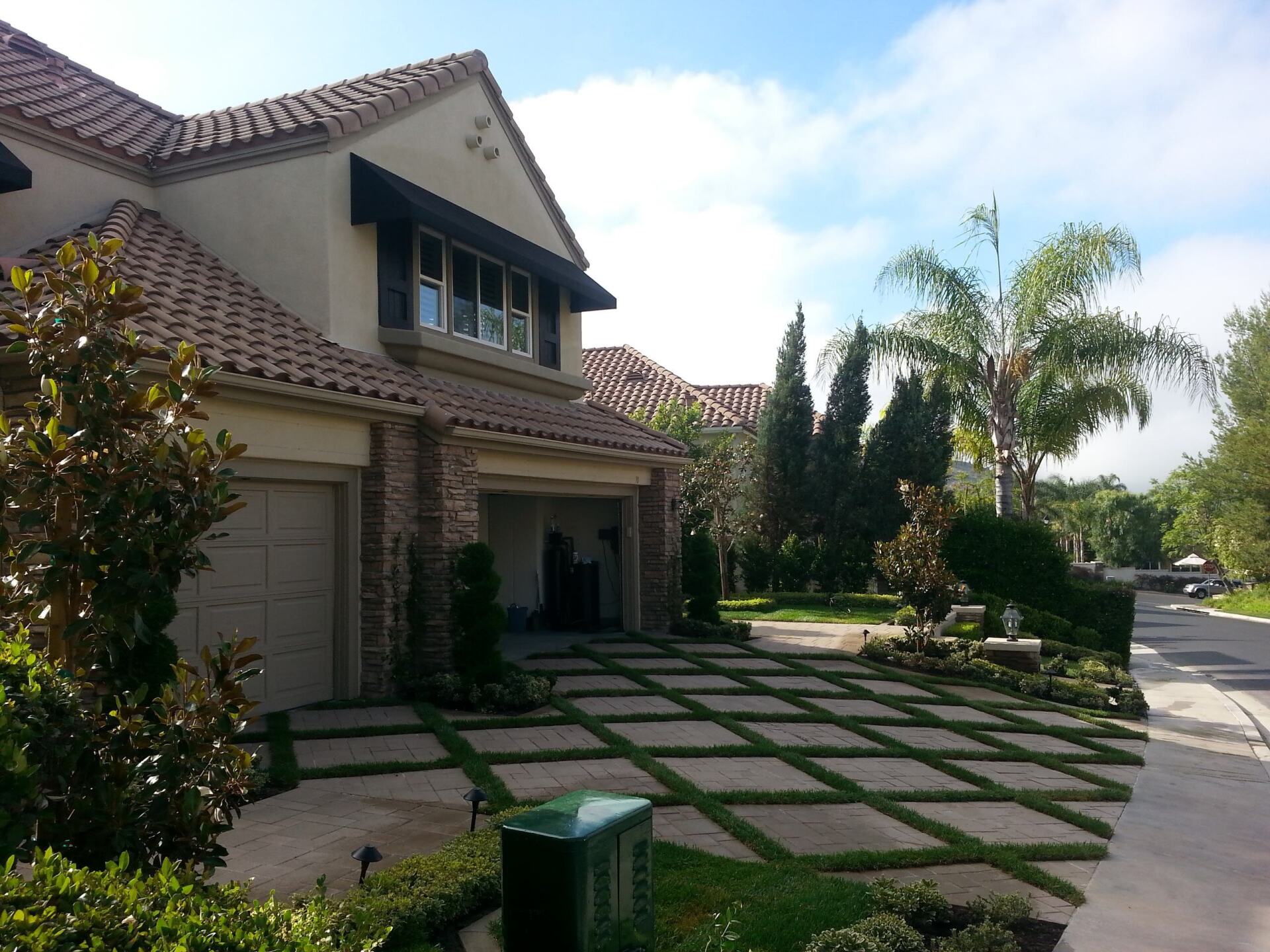 House with a grid driveway of grass and pavers, with a black awning.