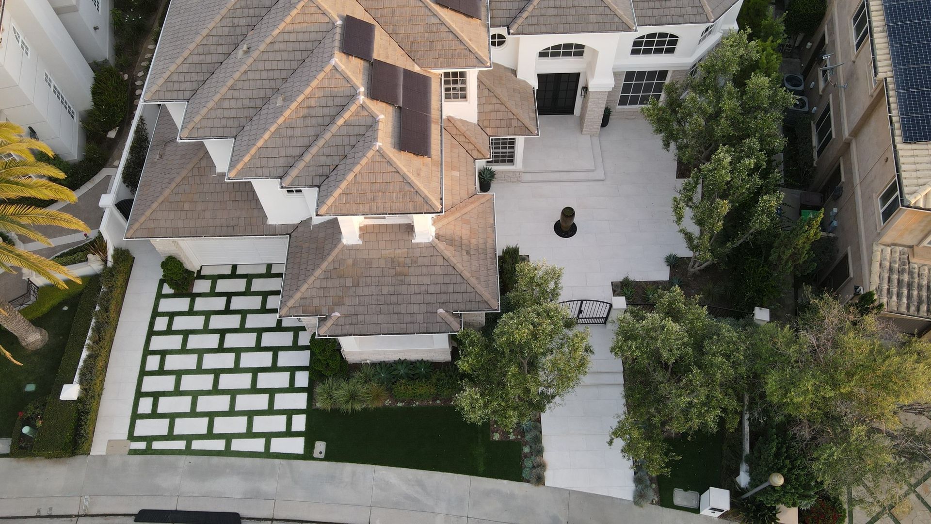 Aerial view of a luxury house with white exterior, brown roof, large driveway, and green landscaping.