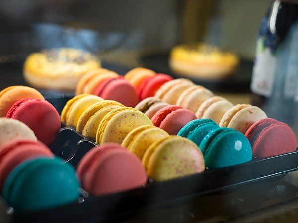 Una bandeja de macarons de colores sobre una mesa con una botella de vino al fondo.